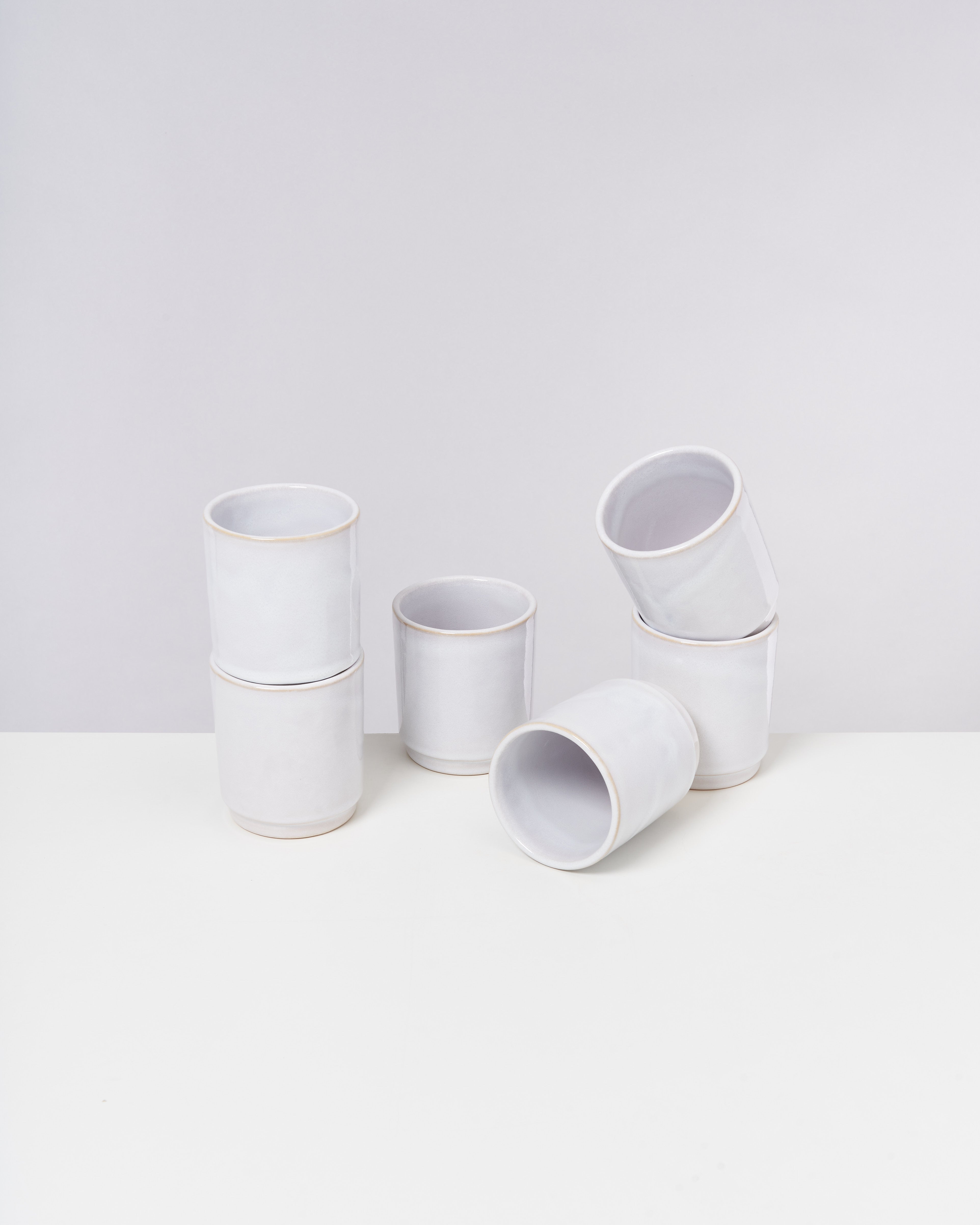Sechs weiße Keramikbecher auf einem weißen Hintergrund, drei stapeln sich, drei liegen seitlich.