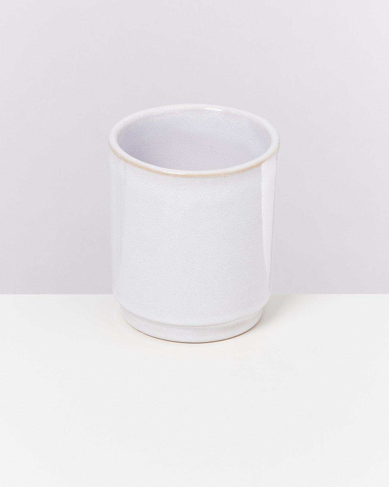 Weißer Keramikbecher mit schlichtem Design auf einem weißen Hintergrund.