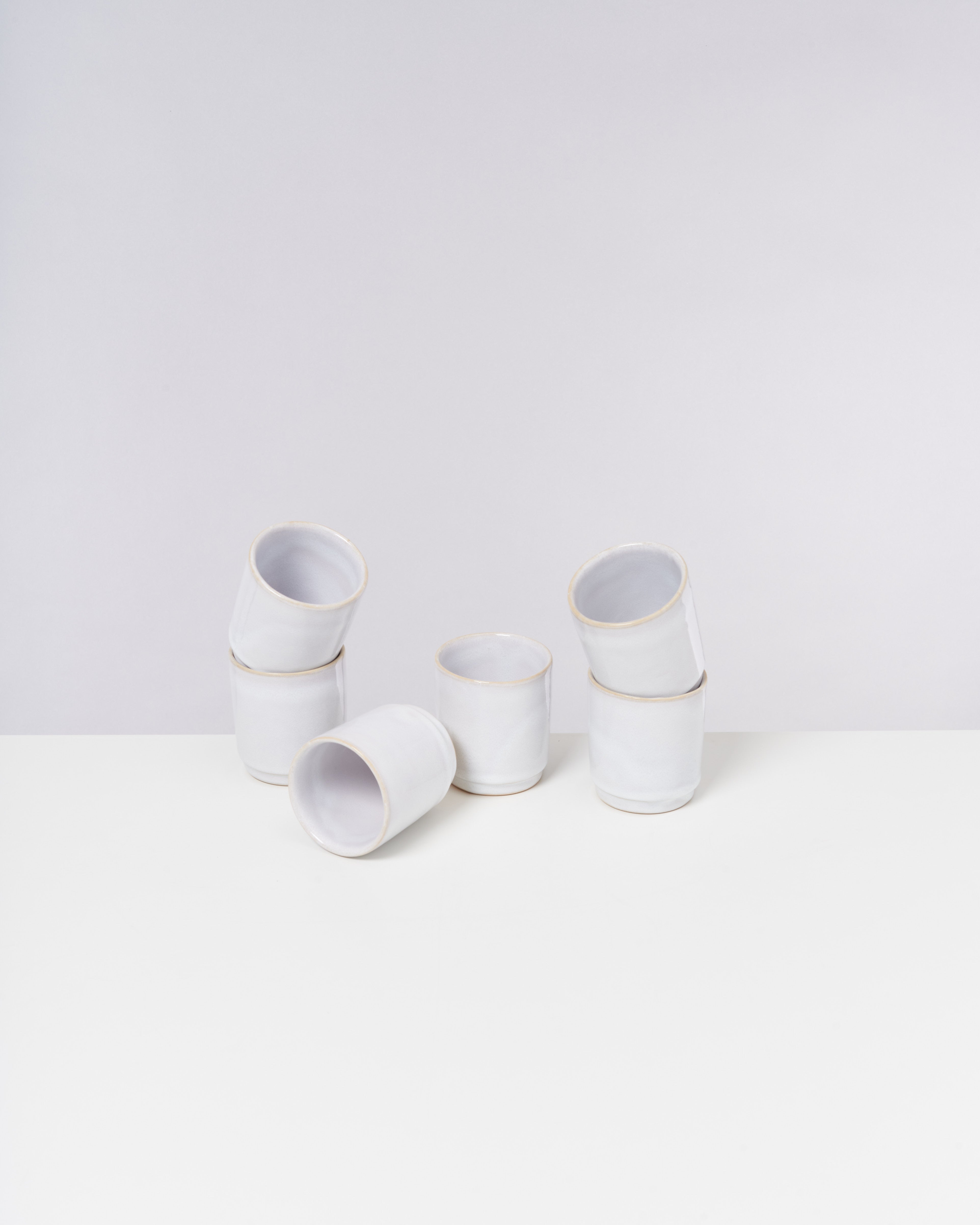 Sechs weiße Keramikbecher auf einer weißen Oberfläche, teils gestapelt, teils liegend.