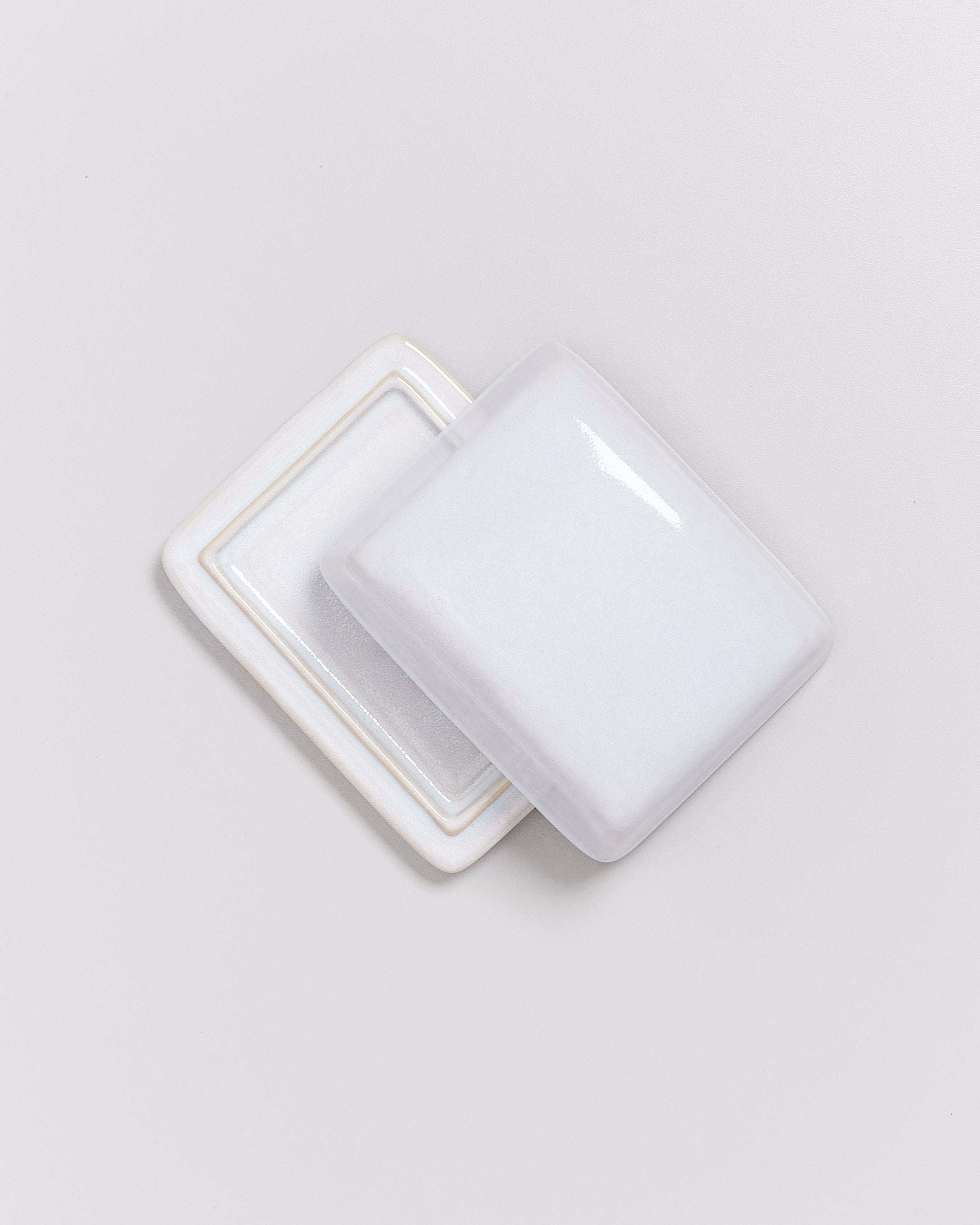 Zwei rechteckige, glänzende, weiße Keramikplatten, leicht versetzt aufeinander gestapelt, auf einem grauen Hintergrund.
