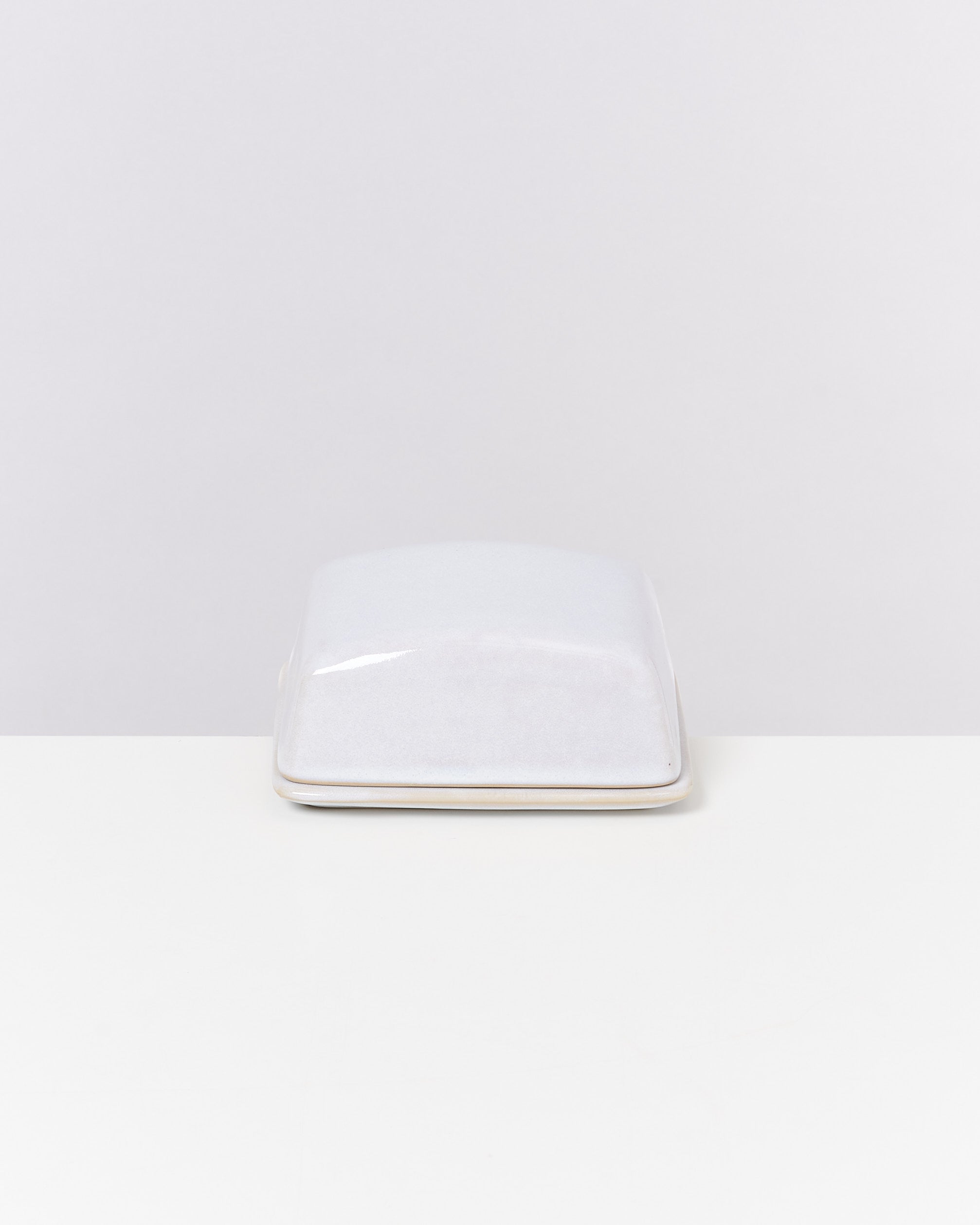 Weiße rechteckige Keramikbutterdose mit Deckel auf hellem Untergrund.