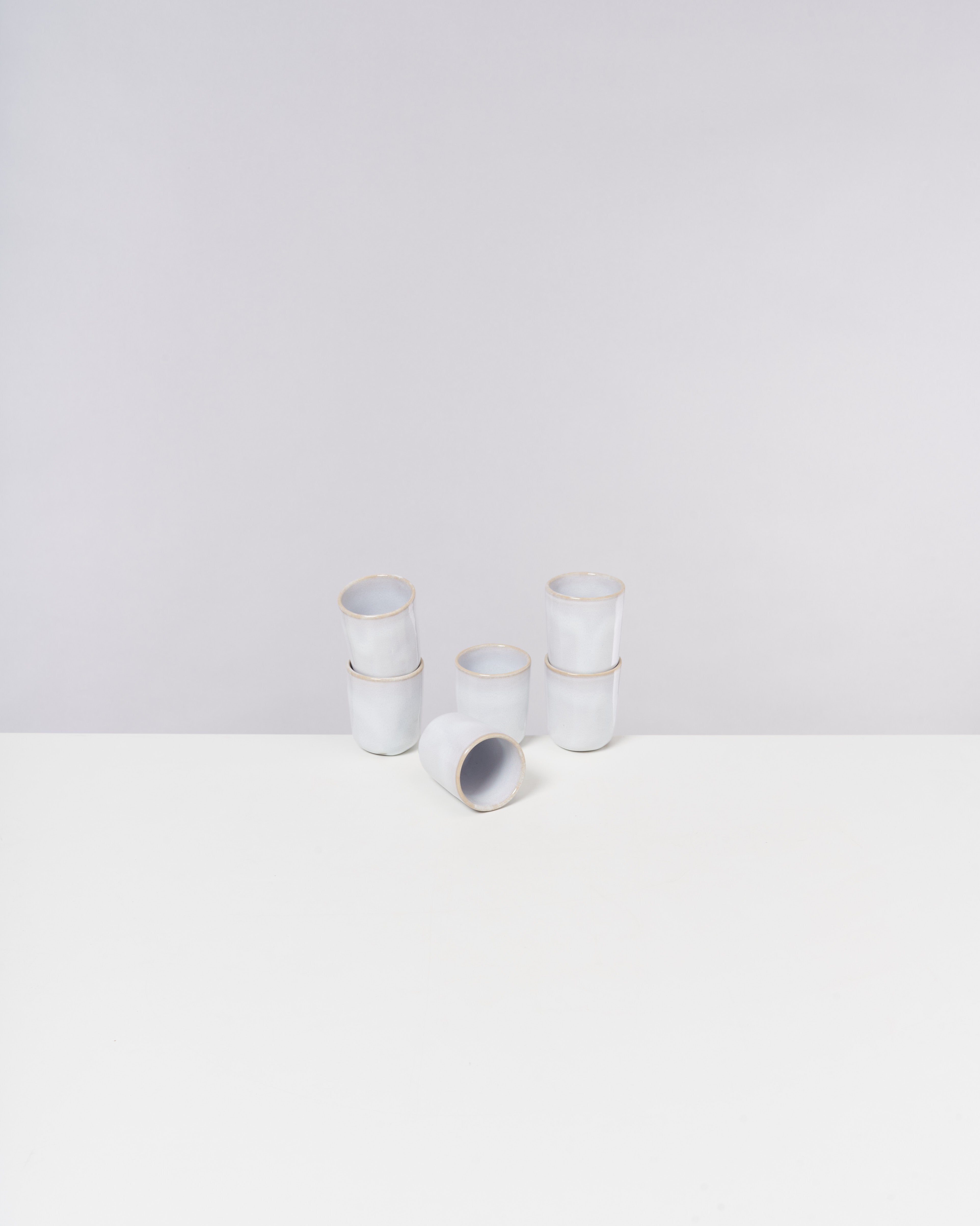 Sechs gestapelte weiße Keramiktassen auf einem weißen Tisch vor einer hellgrauen Wand.