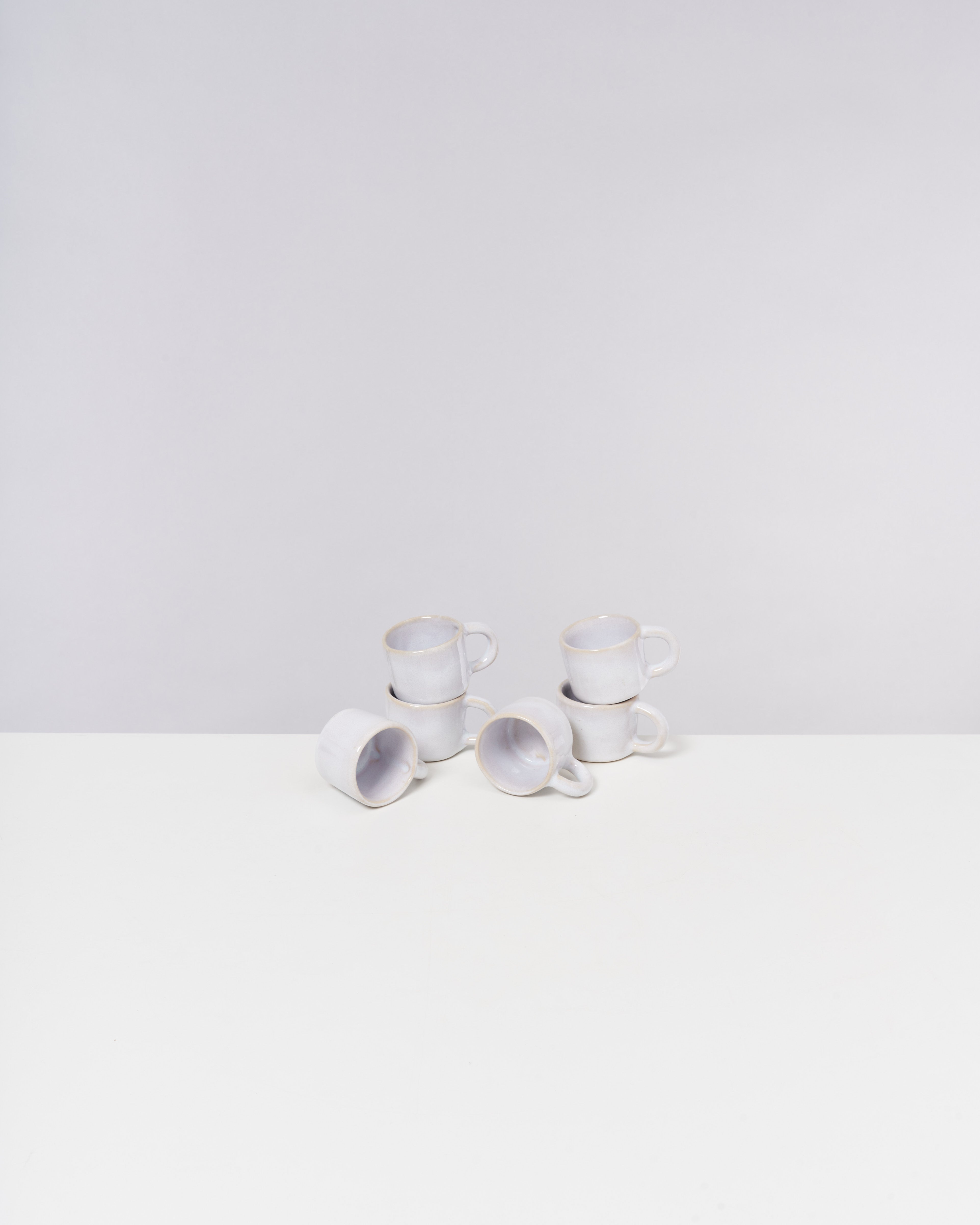 Sechs weiße Tassen mit Henkeln sind auf einem weißen Tisch gestapelt.
