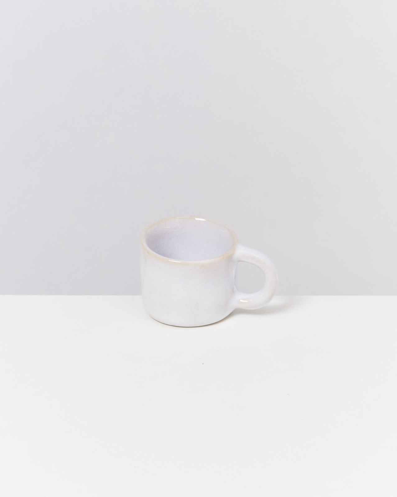 Weiße Keramiktasse mit Henkel auf einem weißen Tisch vor grauem Hintergrund.