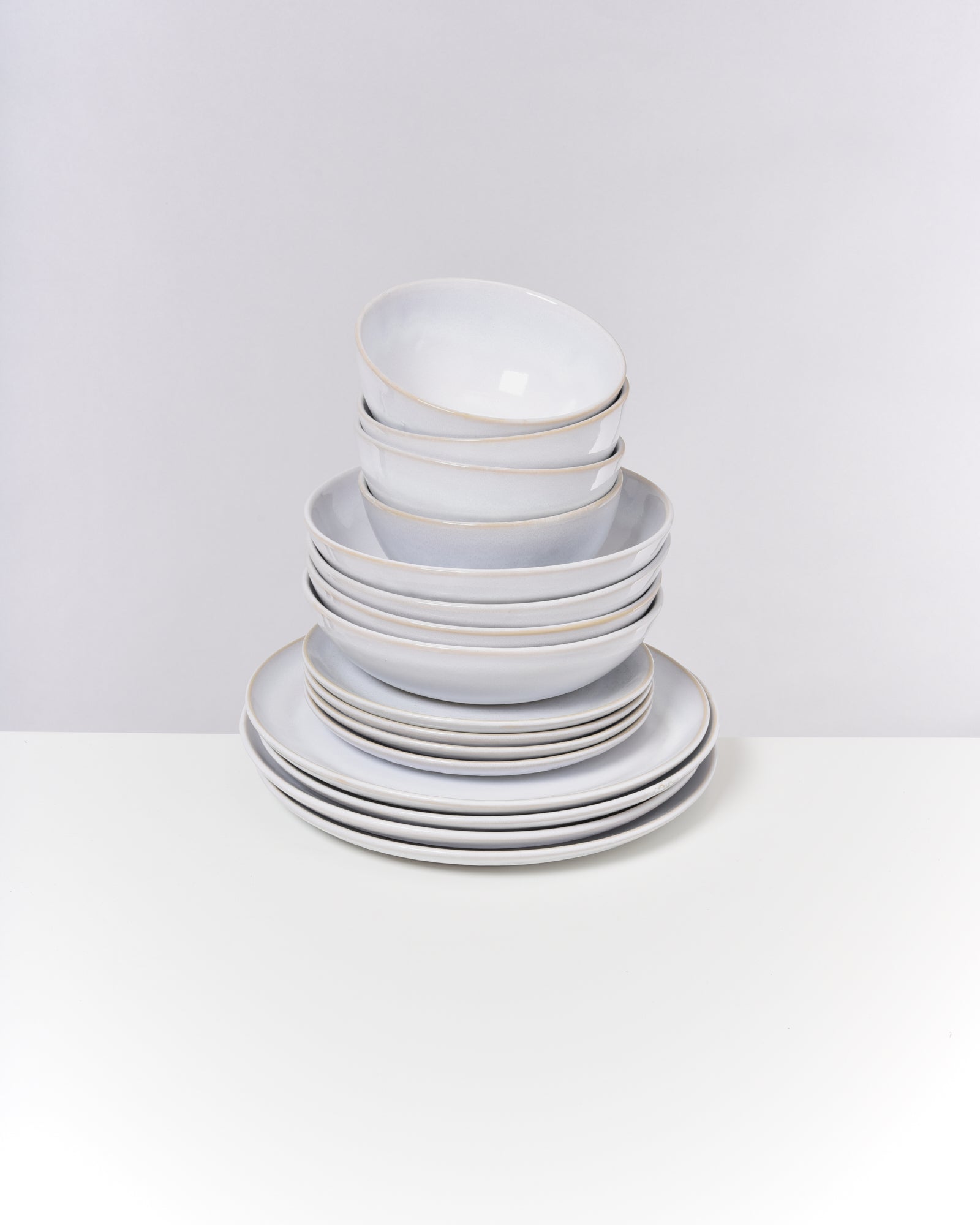 Gestapeltes weißes Keramikgeschirr auf einem weißen Tisch vor einem neutralen Hintergrund.