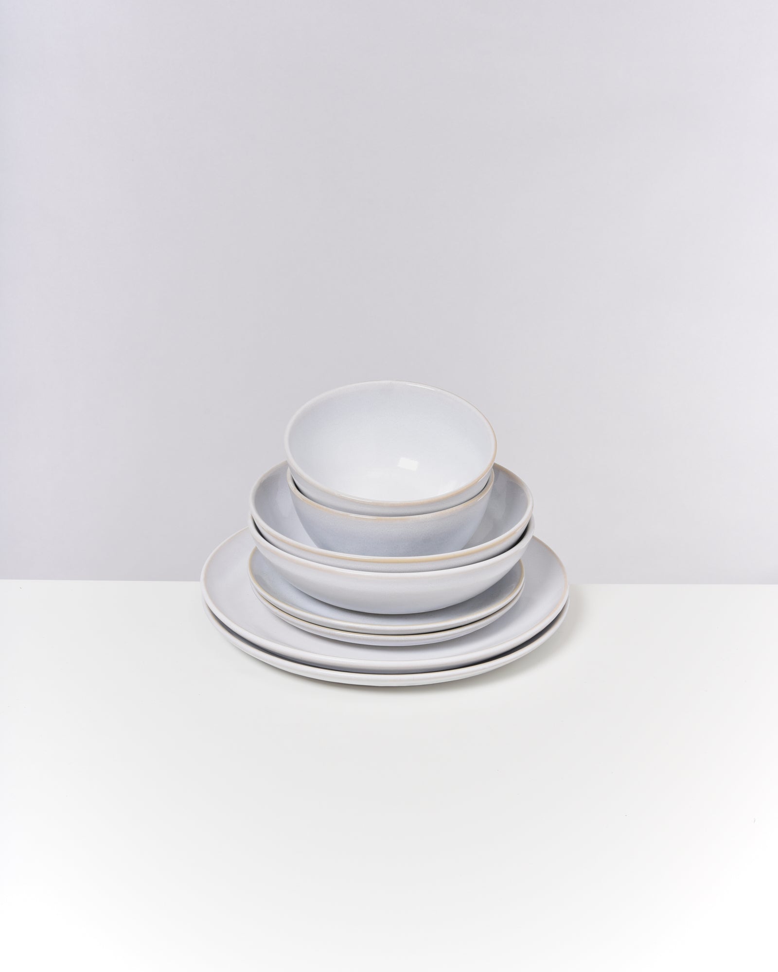 Ein Stapel aus weißem Geschirr mit zwei Schüsseln und zwei Tellern auf einem weißen Hintergrund.