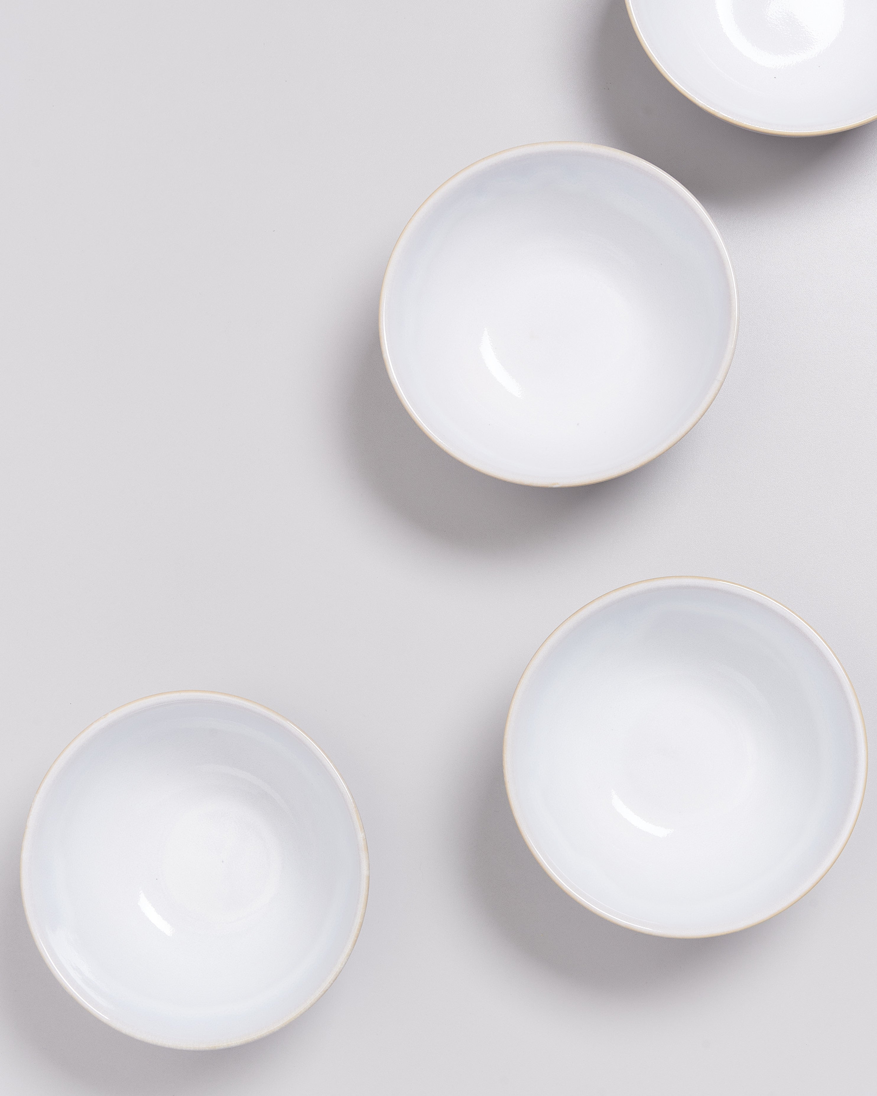 Vier weiße Schüsseln sind diagonal auf einer grauen Oberfläche angeordnet.