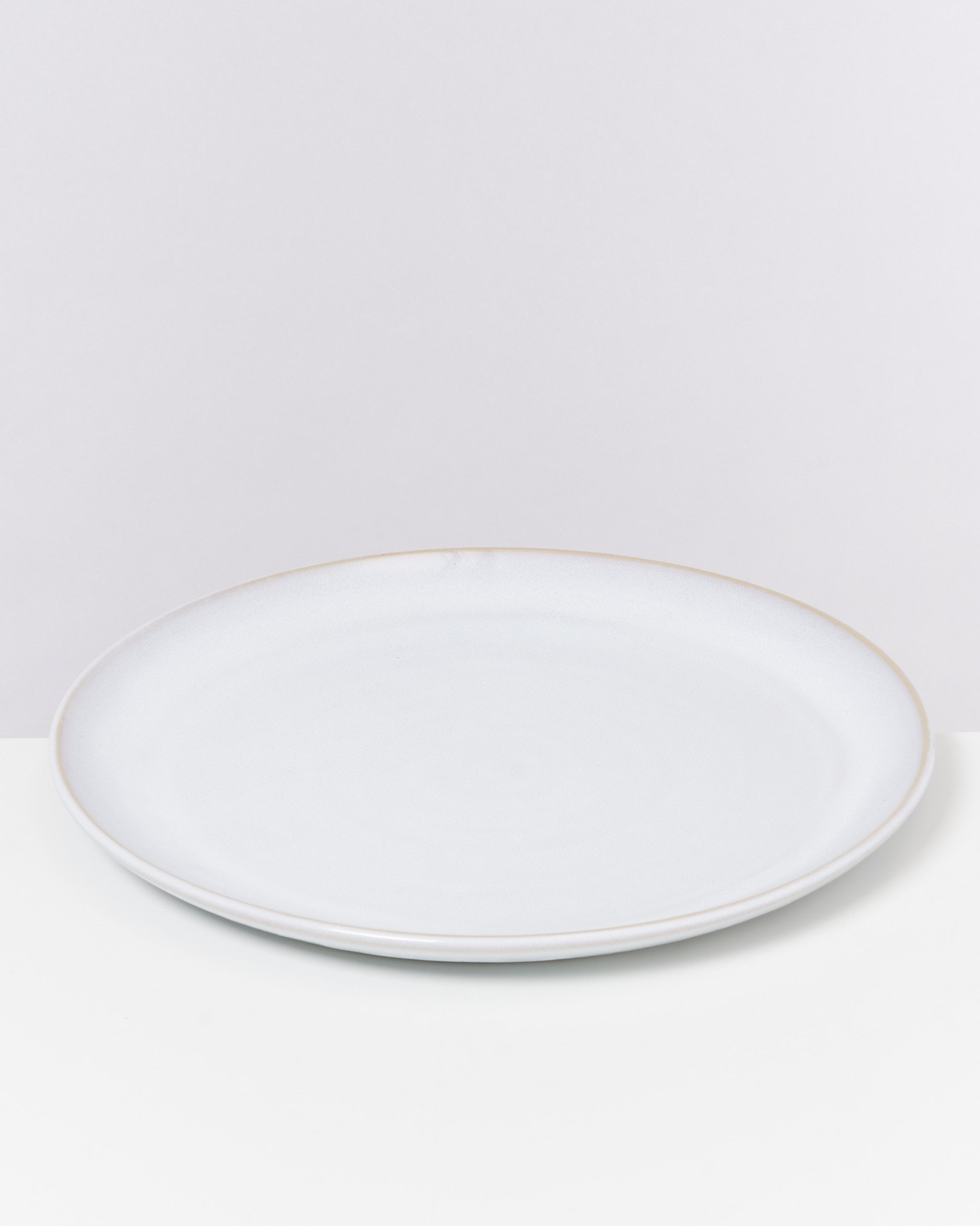 Weiße, runde, leere Keramikplatte auf hellem Hintergrund.