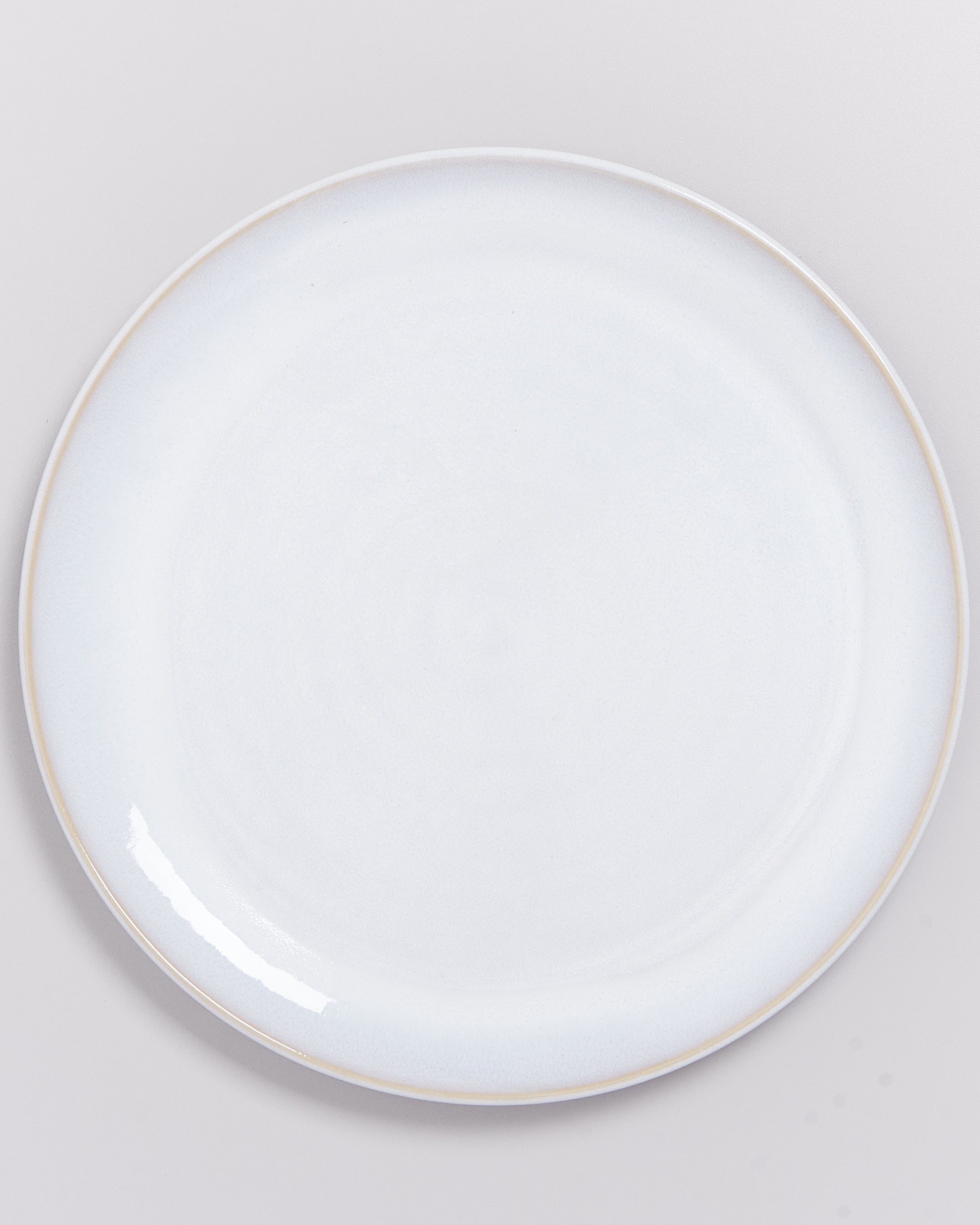Weiße, runde Keramikplatte auf einem hellgrauen Hintergrund.