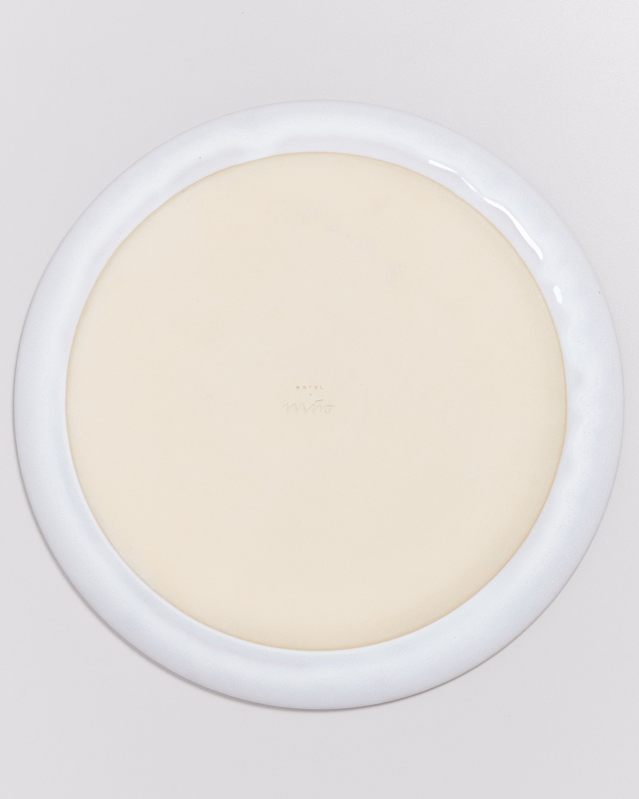 Unterseite eines runden Keramiktellers mit breitem weißem Rand und glatter beiger Mitte.