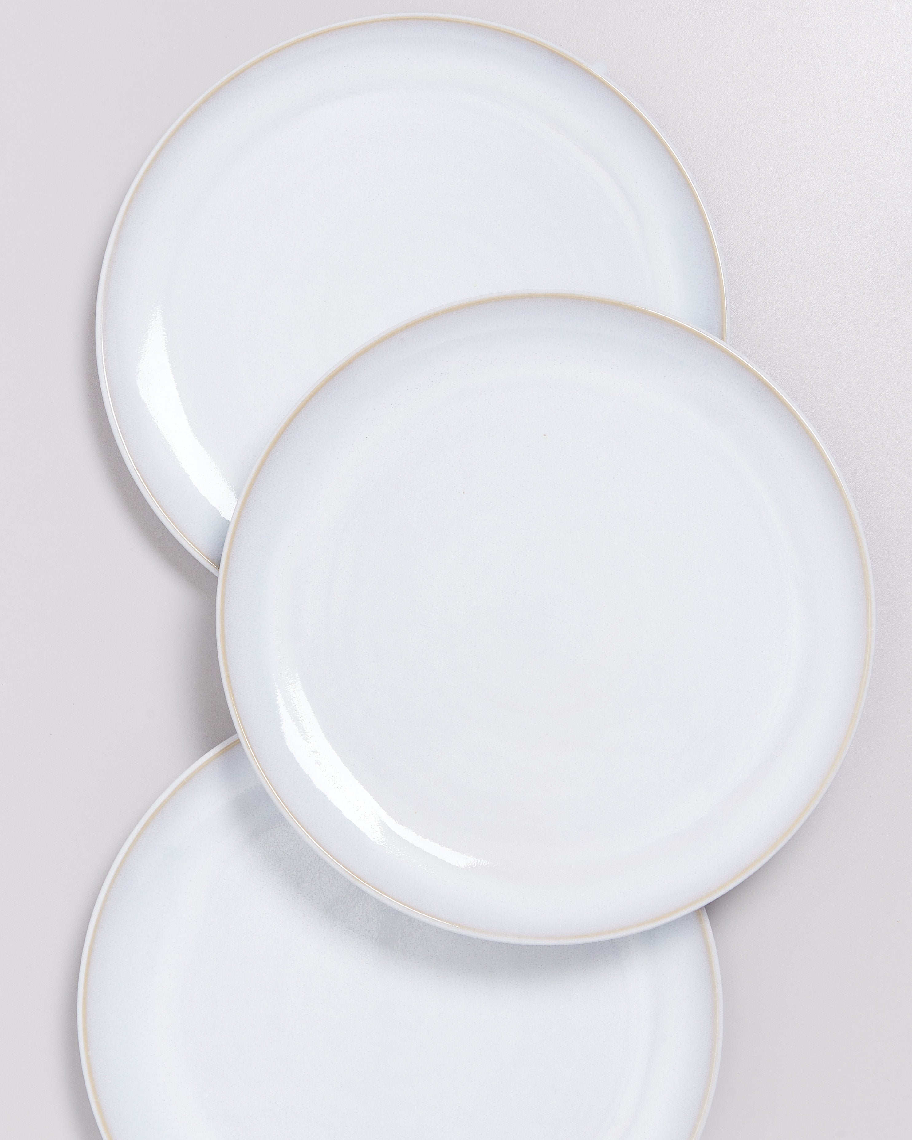 Drei weiße, sich leicht überlappende Teller vor einem grauen Hintergrund.
