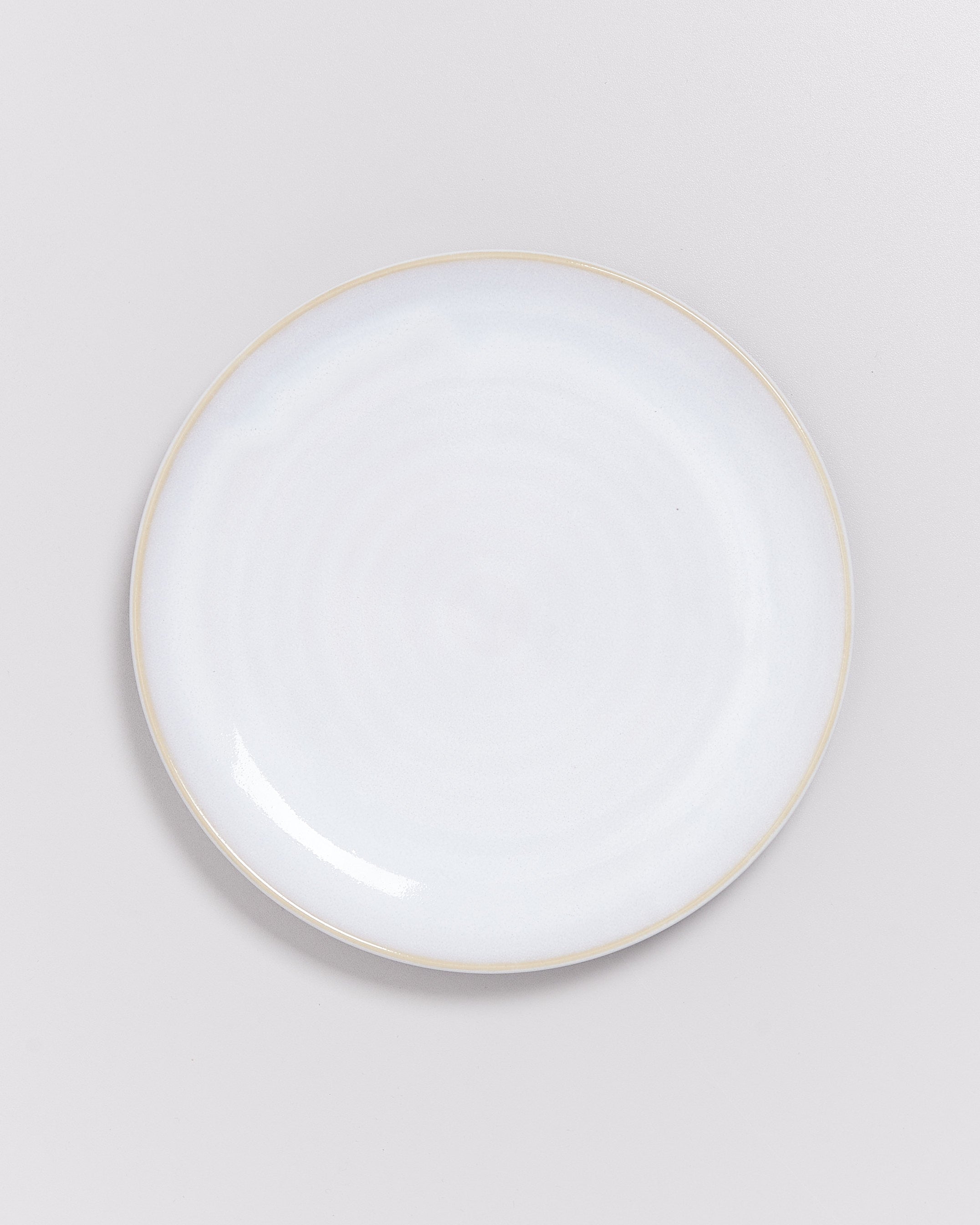 Ein weißer, runder Keramikteller auf einem hellgrauen Hintergrund.