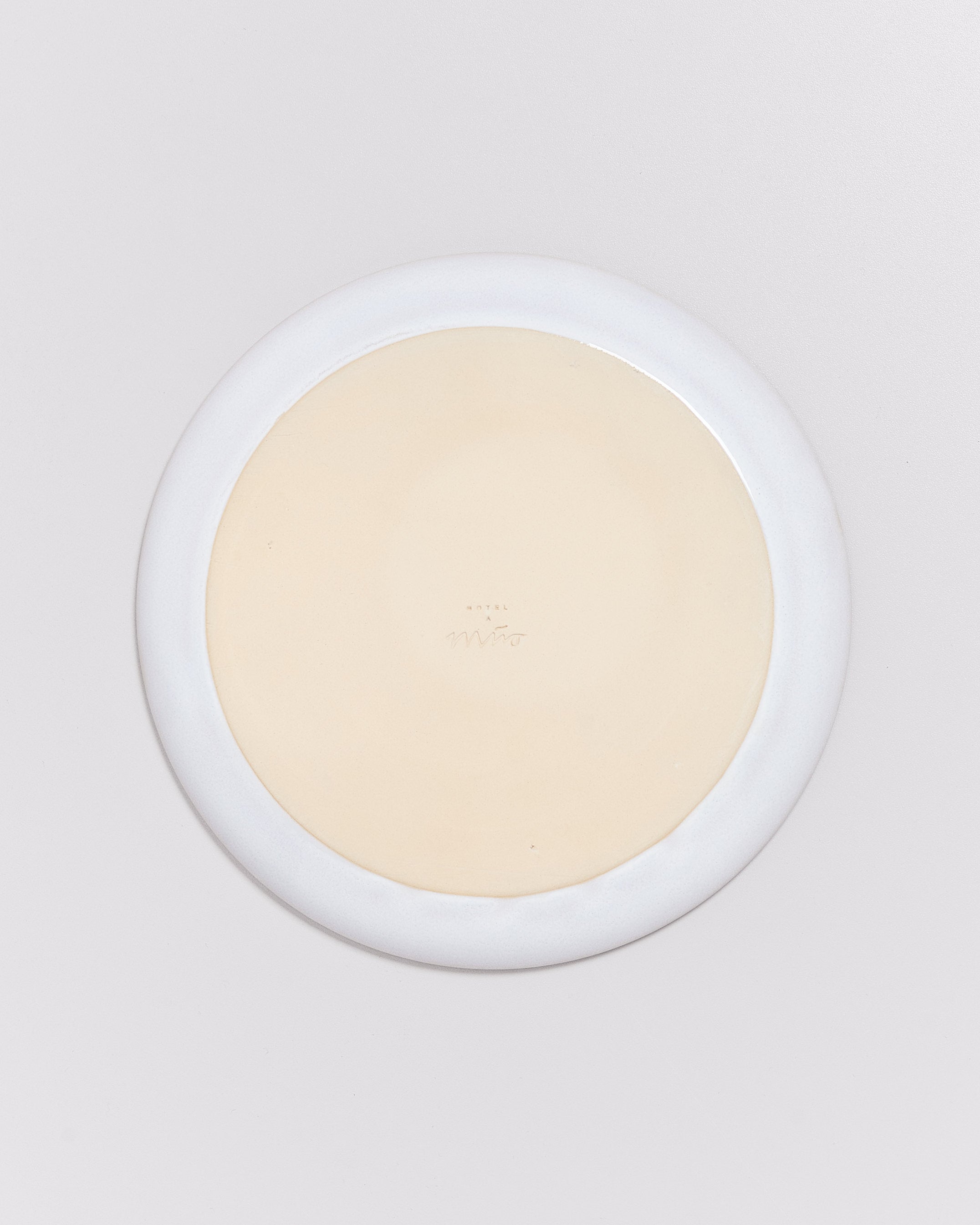 Rückseite eines weißen Tellers mit einem cremefarbenen Zentrum vor einem grauen Hintergrund.