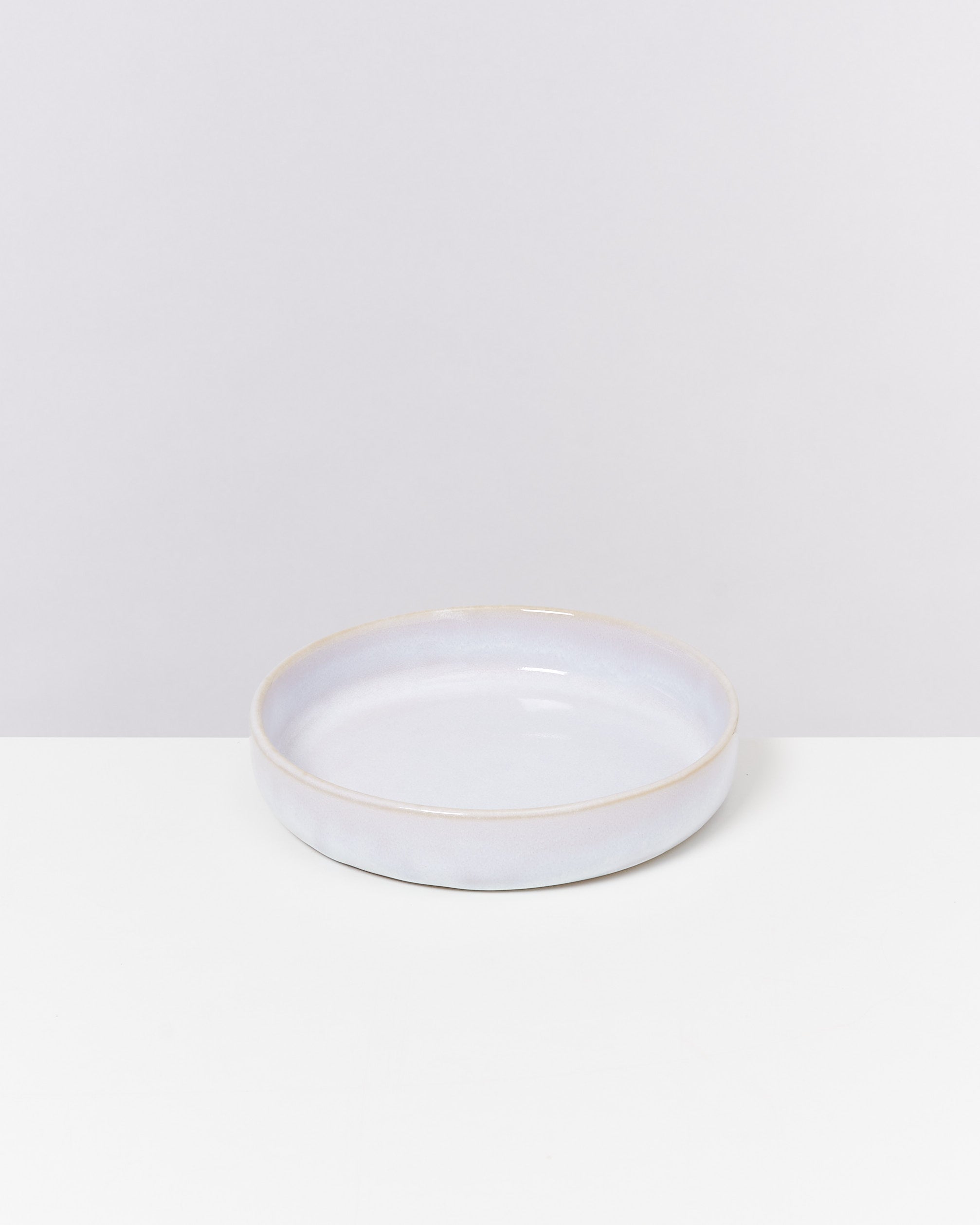 Eine flache, runde, pastellfarbene Keramikschale auf einem weißen Tisch vor einem hellgrauen Hintergrund.