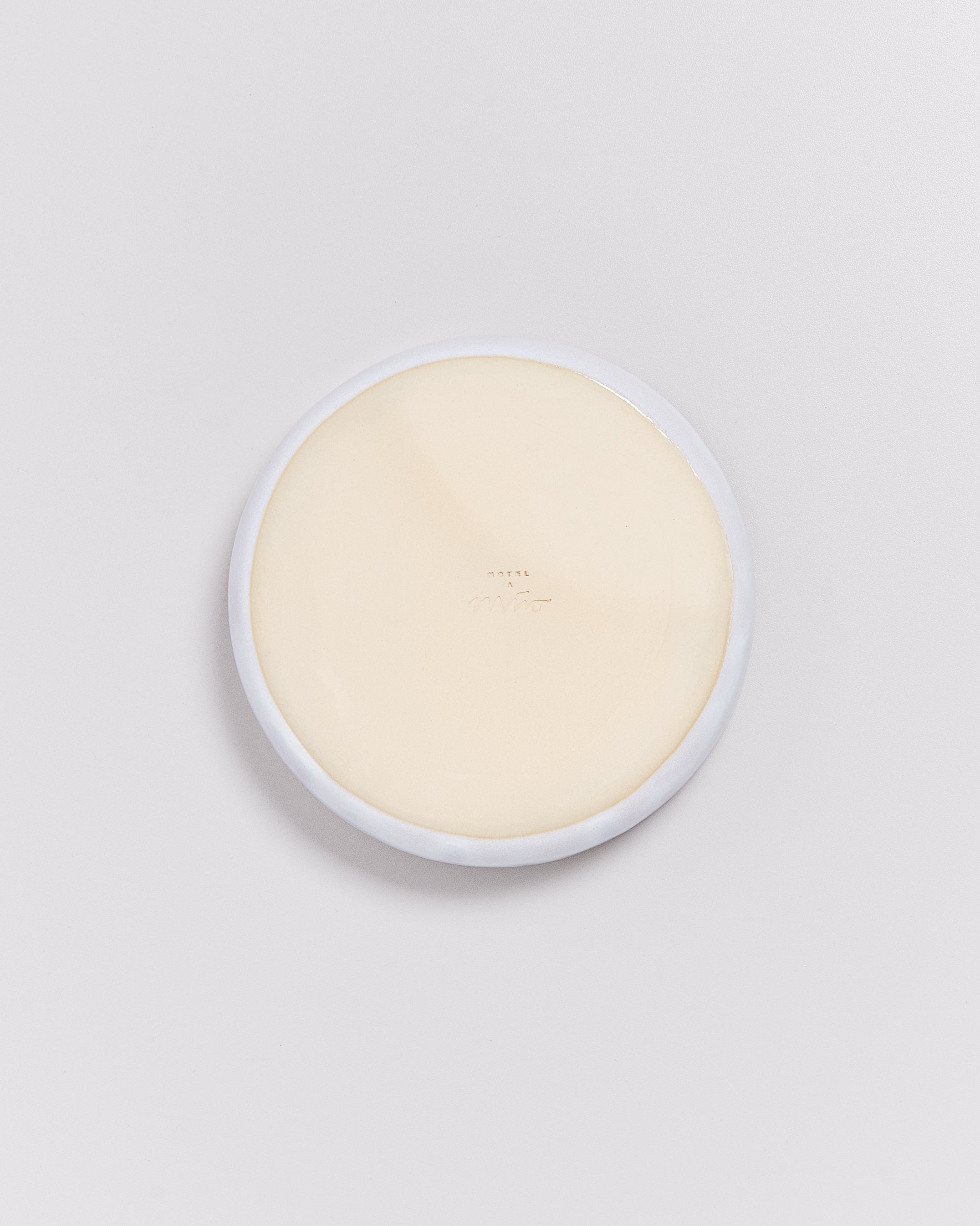 Runder, beigefarbener Teller mit erhabener Schrift auf weißem Hintergrund.