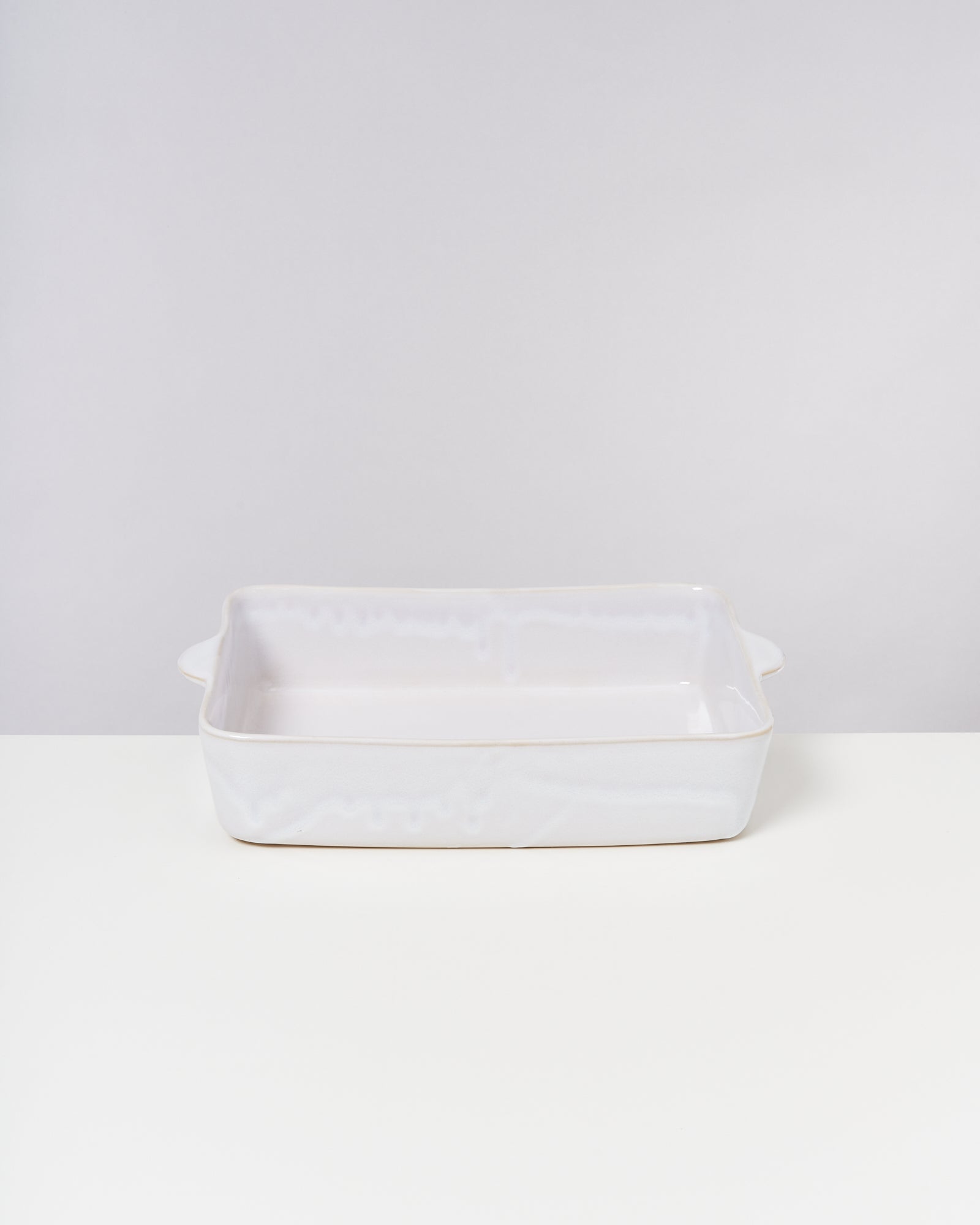 Weiße, rechteckige Keramik-Auflaufform mit Griffen auf einem weißen Untergrund vor grauem Hintergrund.