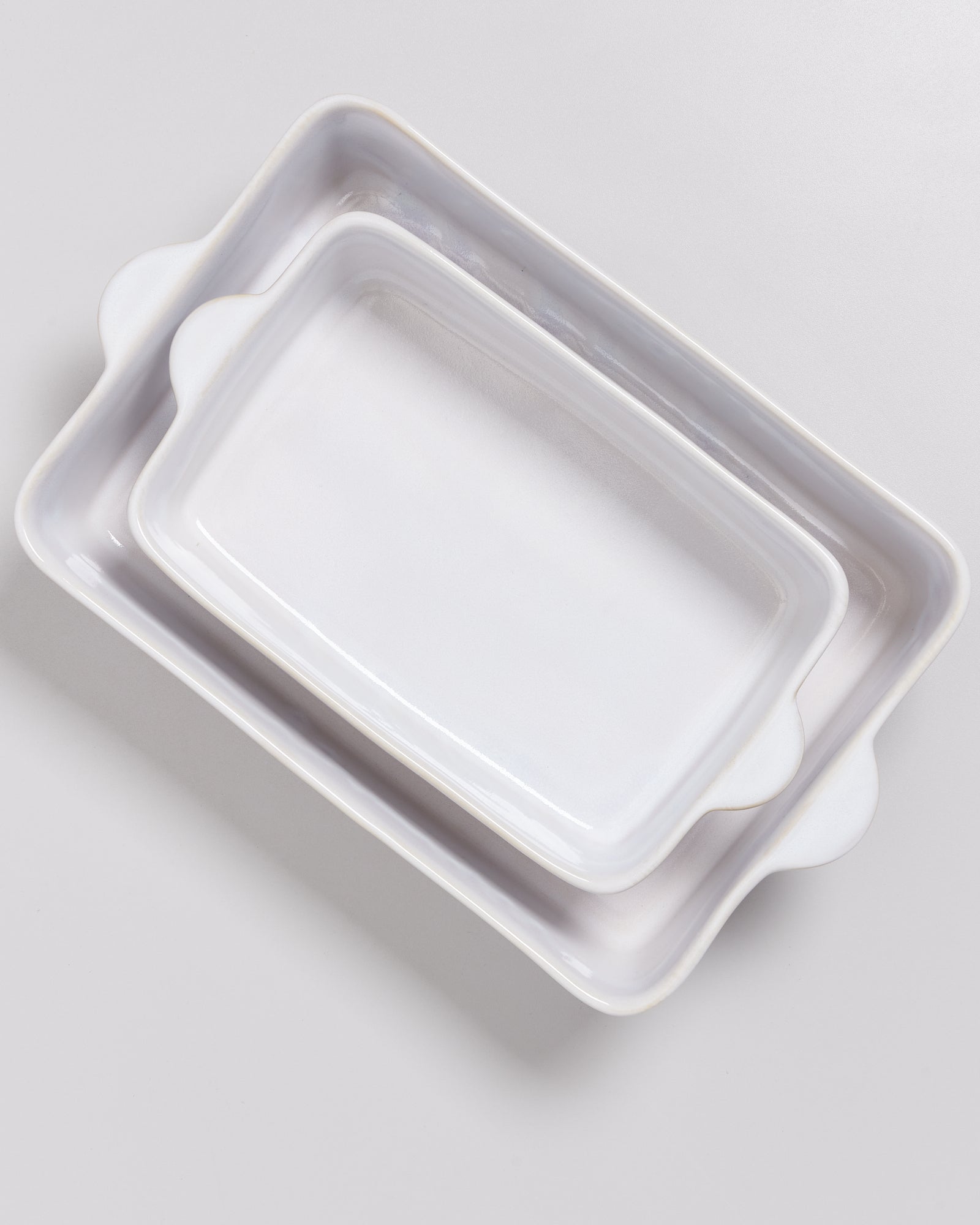 Zwei ineinander gestapelte, rechteckige, weiße Keramik-Auflaufformen auf einer grauen Oberfläche.