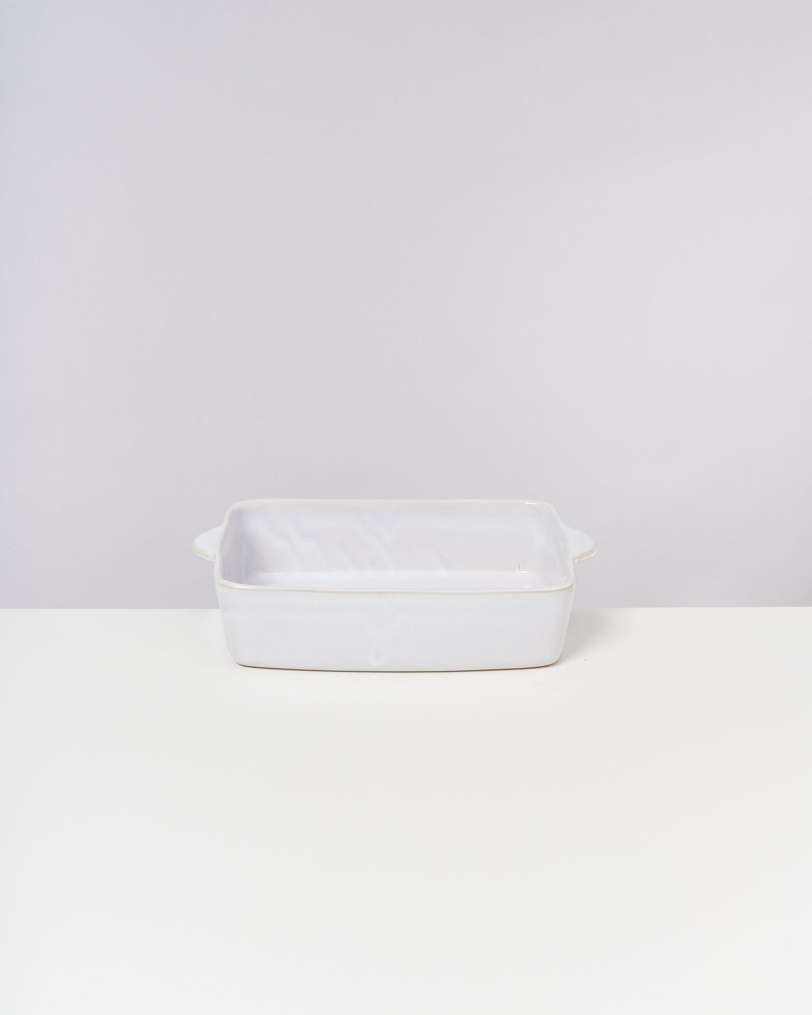 Weiße rechteckige Backform auf einem weißen Untergrund vor grauem Hintergrund.