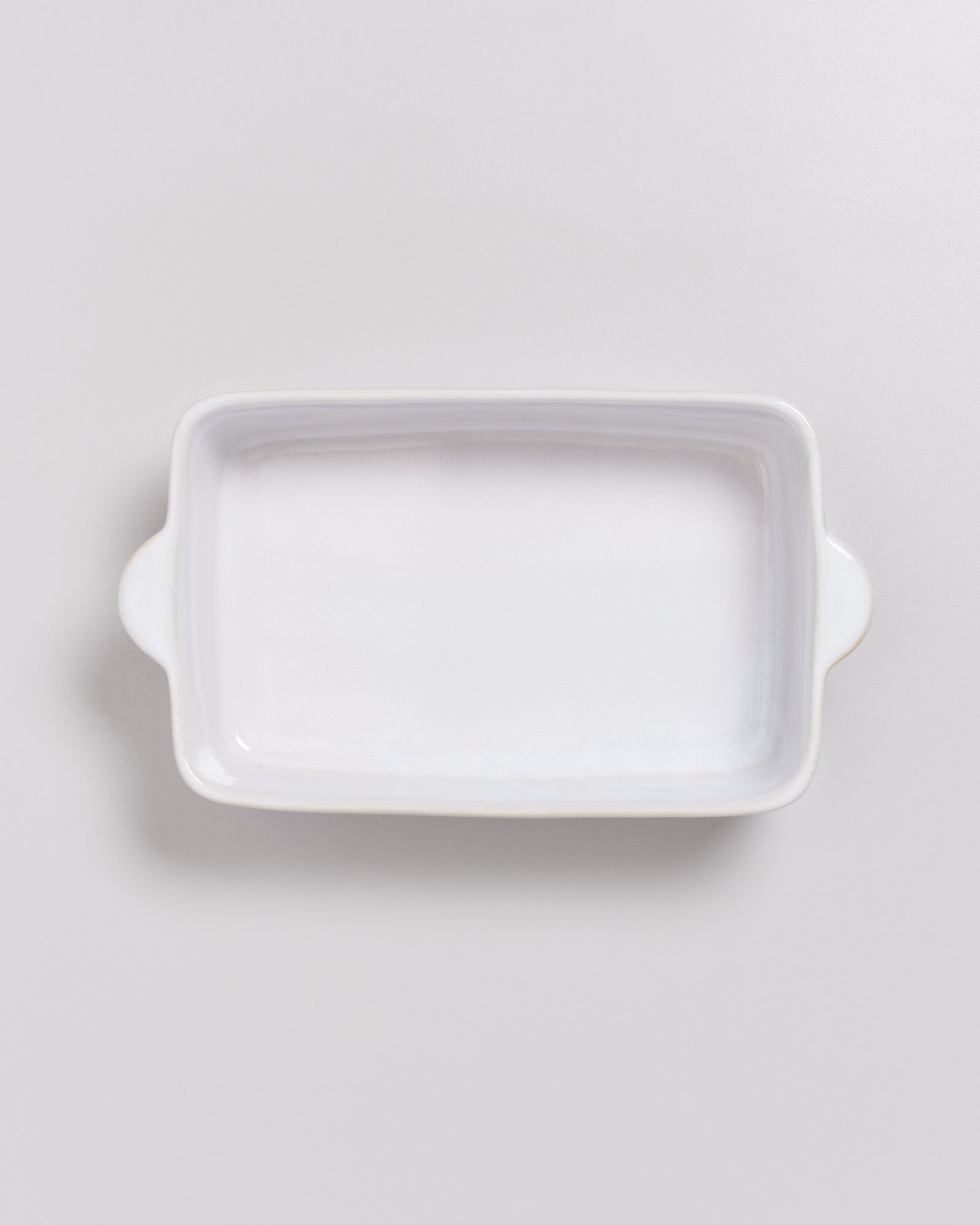 Weiße rechteckige Keramikschale mit Griffen auf einem hellgrauen Hintergrund.