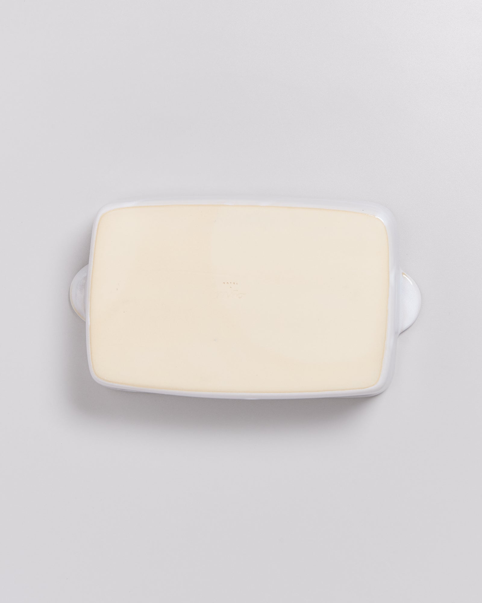 Rechteckige, cremefarbene Keramikplatte mit leicht erhobenem Rand und Griffen, auf hellem Hintergrund.