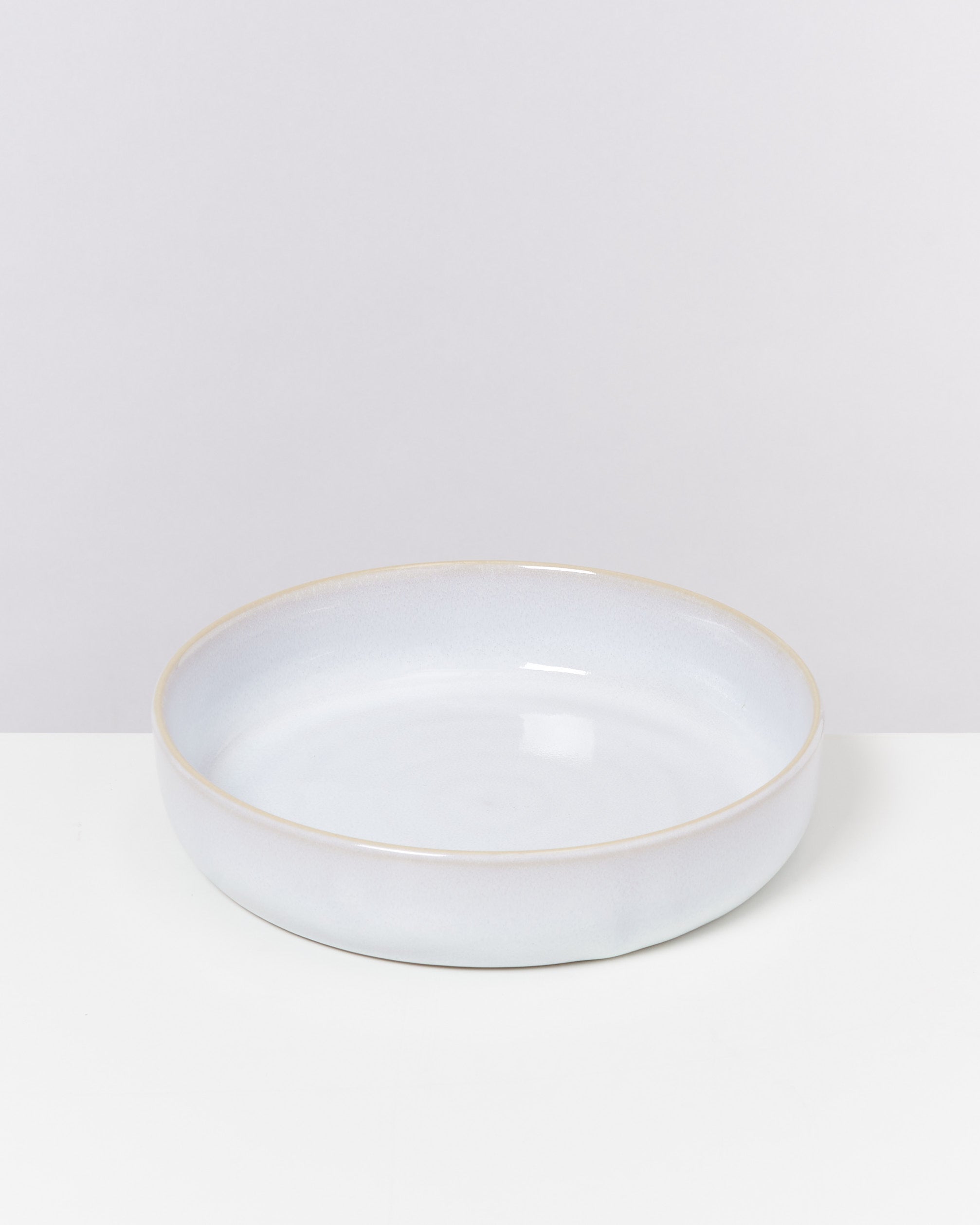 Eine flache, runde, hellgraue Schale mit einem leicht erhabenen Rand steht vor einem neutralen Hintergrund.