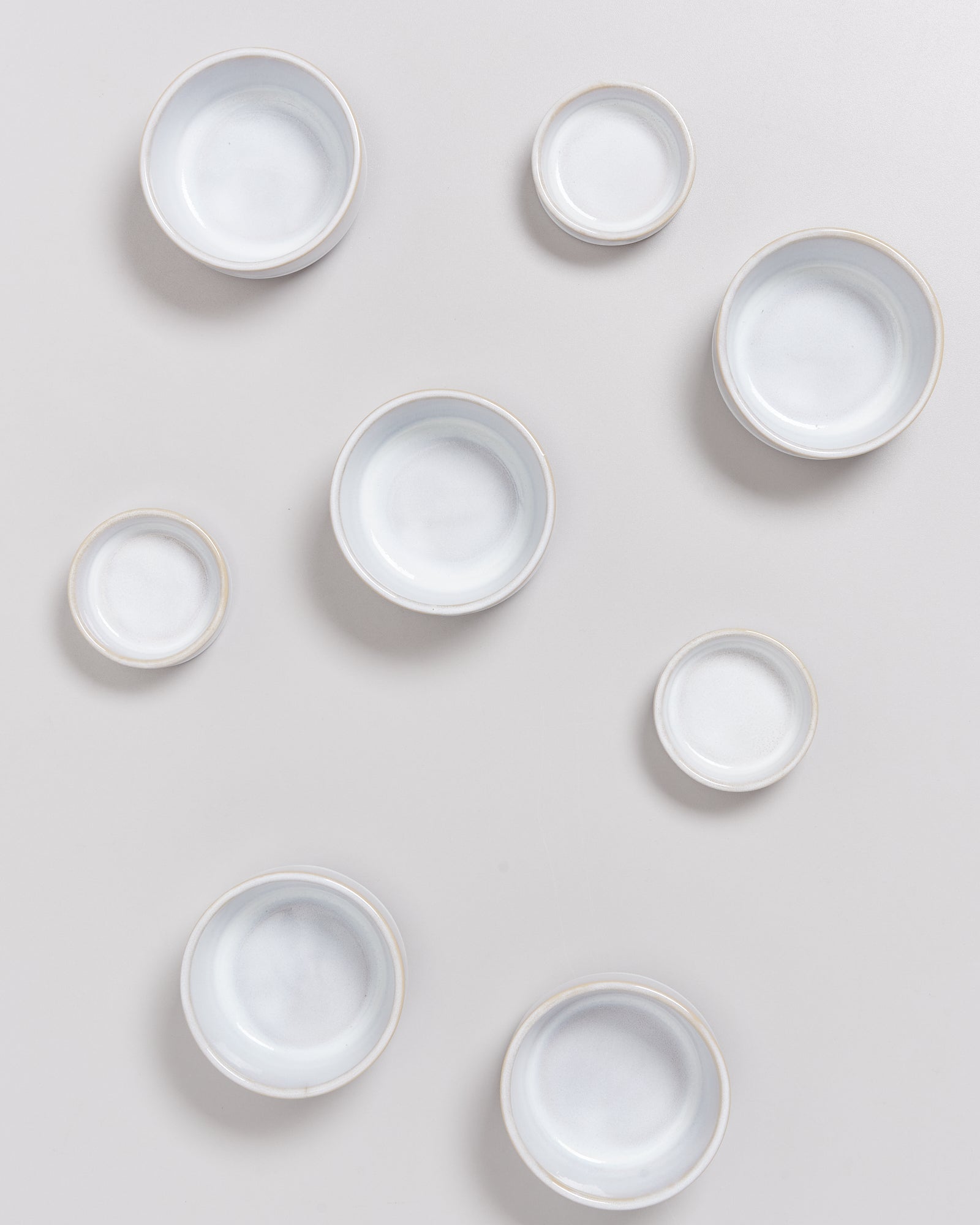 Acht weiße, unterschiedlich große Keramikschalen auf einem hellgrauen Hintergrund.