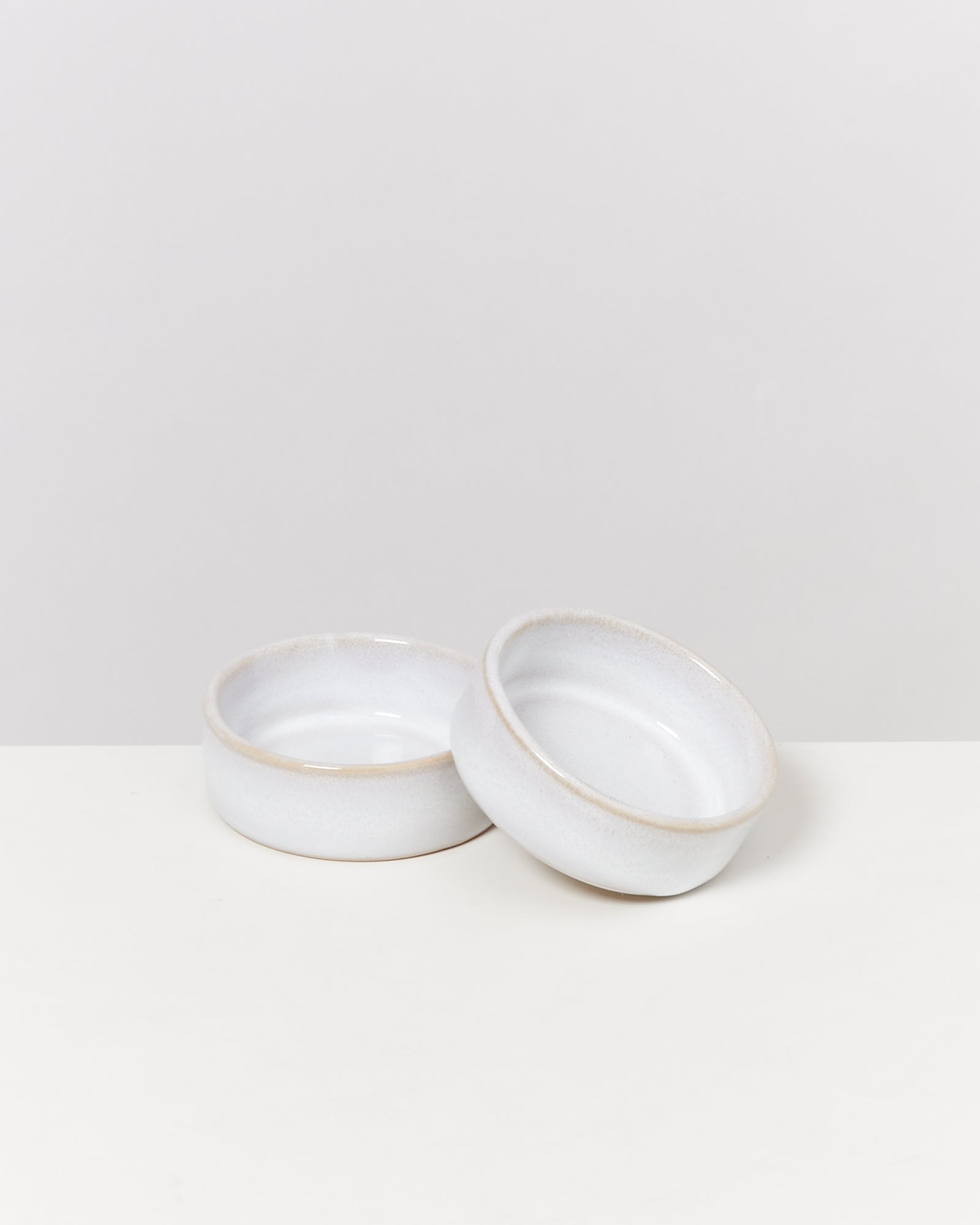Zwei weiße, runde Keramikschalen auf einem hellen Hintergrund, leicht überlappend platziert.