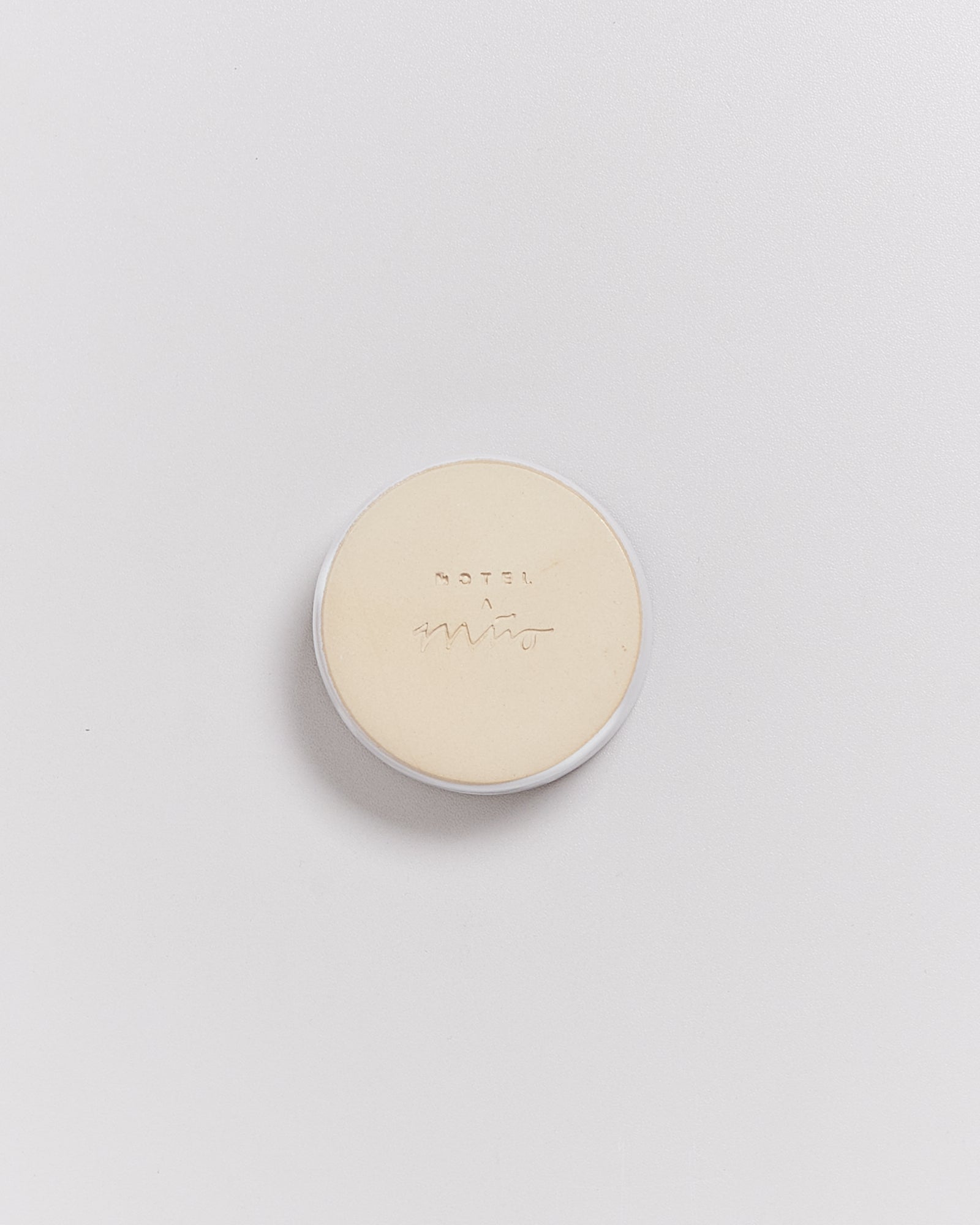 Runder, beiger Deckel mit Aufschrift auf hellem Hintergrund.