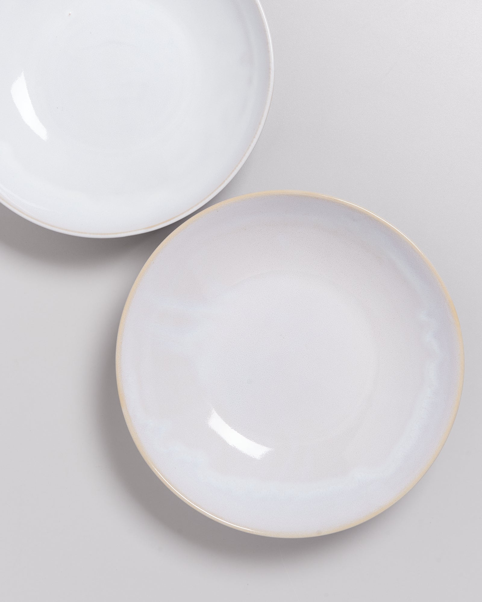 Zwei teilweise überlappende, schlichte weiße Teller auf einer hellgrauen Oberfläche.