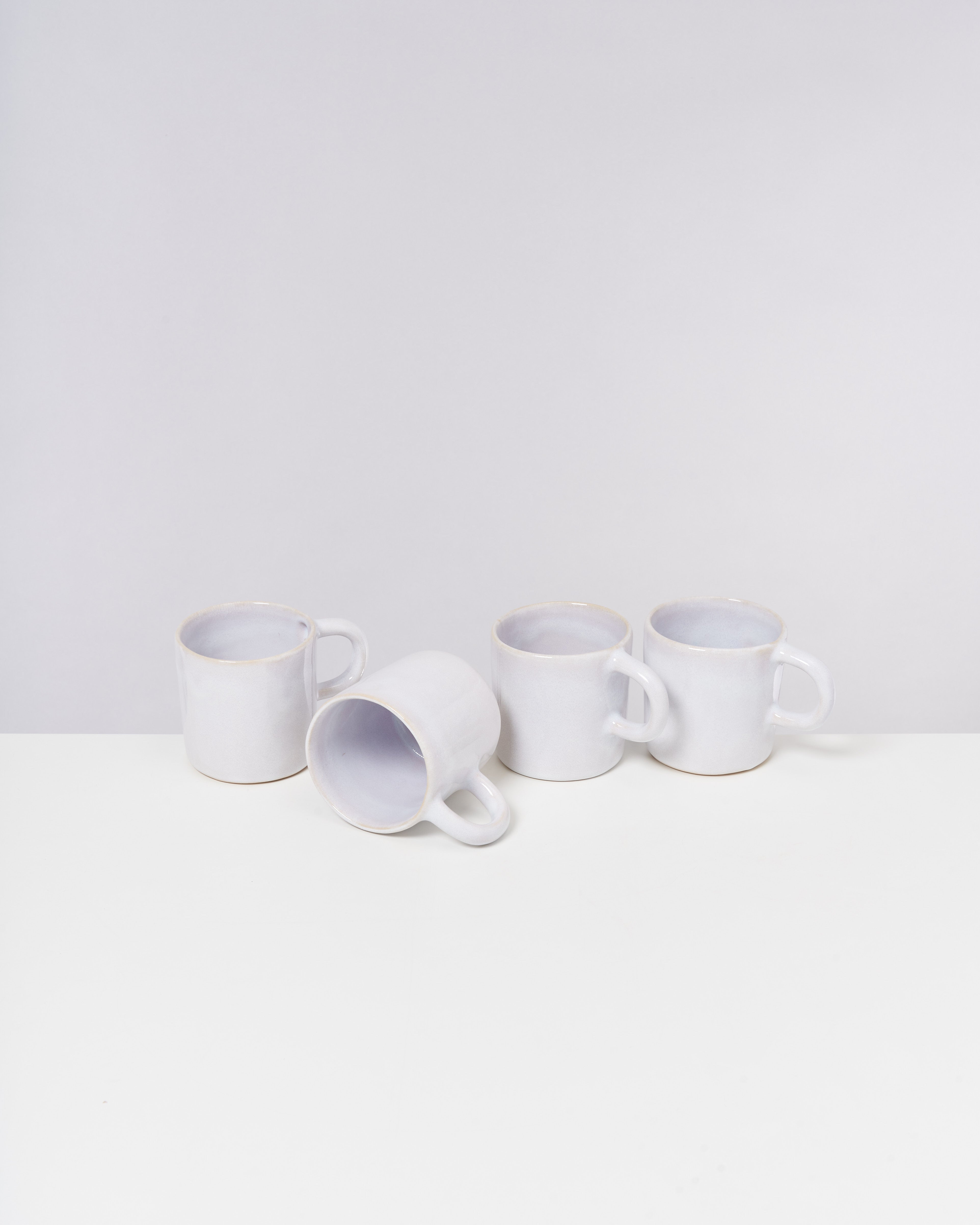 Vier weiße Tassen auf einem weißen Tisch, eine liegt auf der Seite.