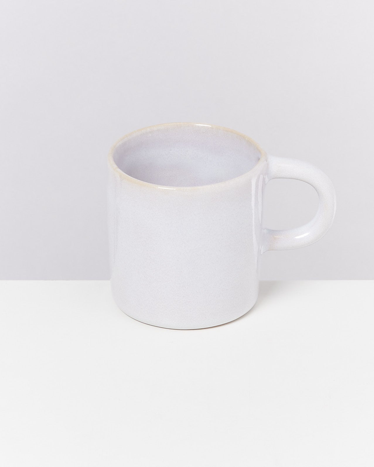 Weiße Keramiktasse mit Henkel steht auf einem weißen Hintergrund.