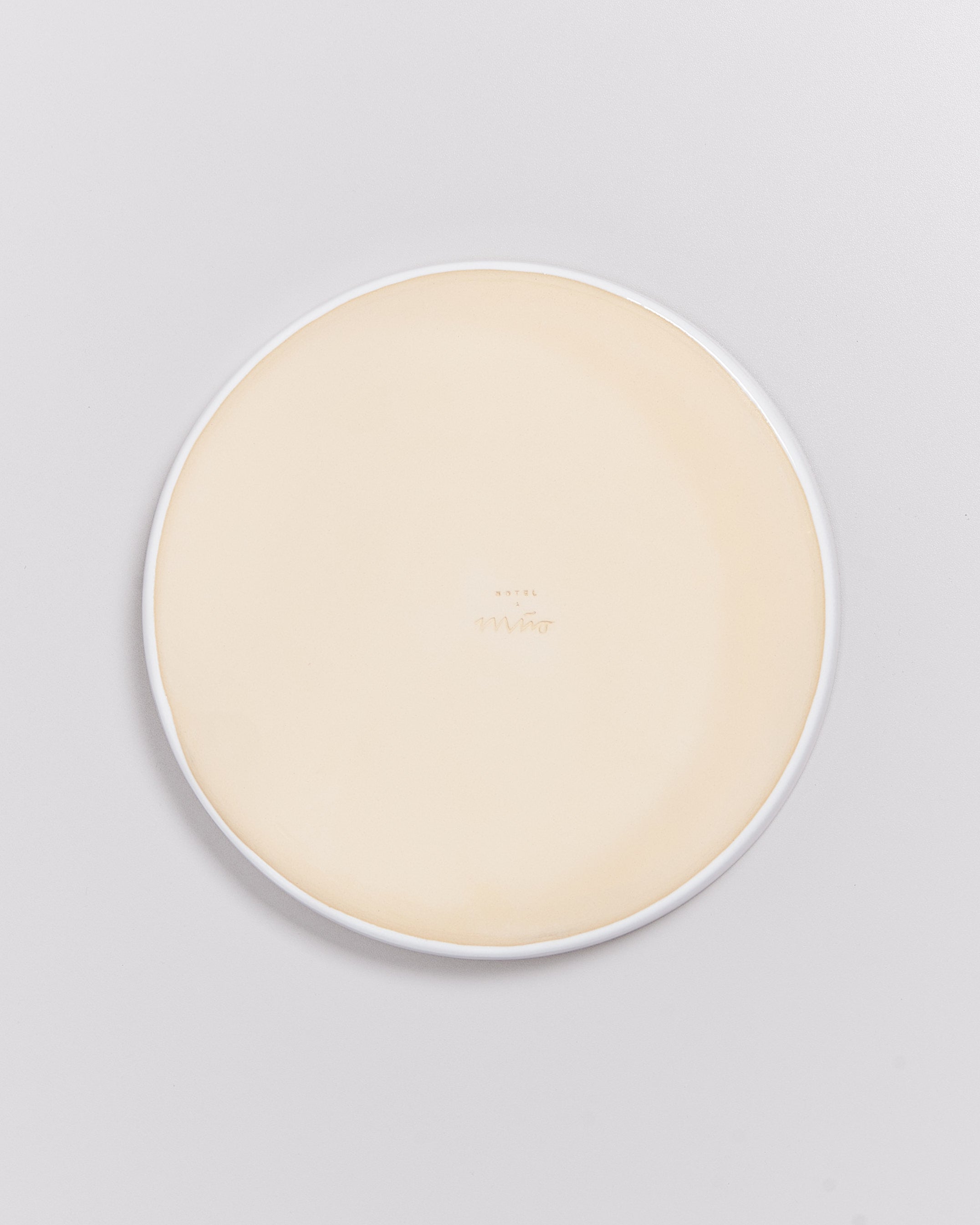 Runde, cremefarbene Keramikplatte mit weißem Rand auf hellem Hintergrund.
