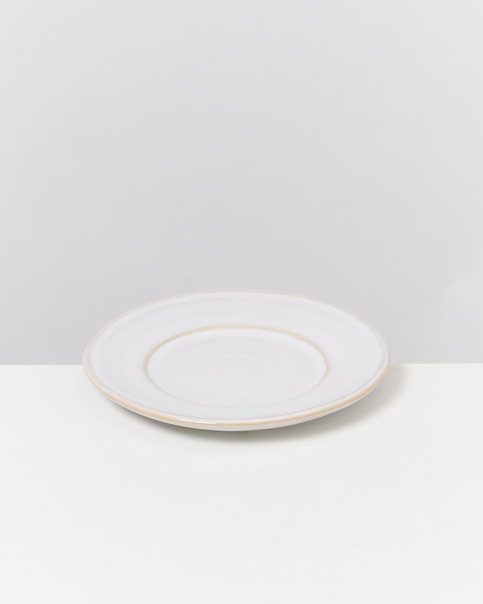 Ein weißer, runder Teller mit leichtem Rand steht auf einer weißen Oberfläche vor einem grauen Hintergrund.