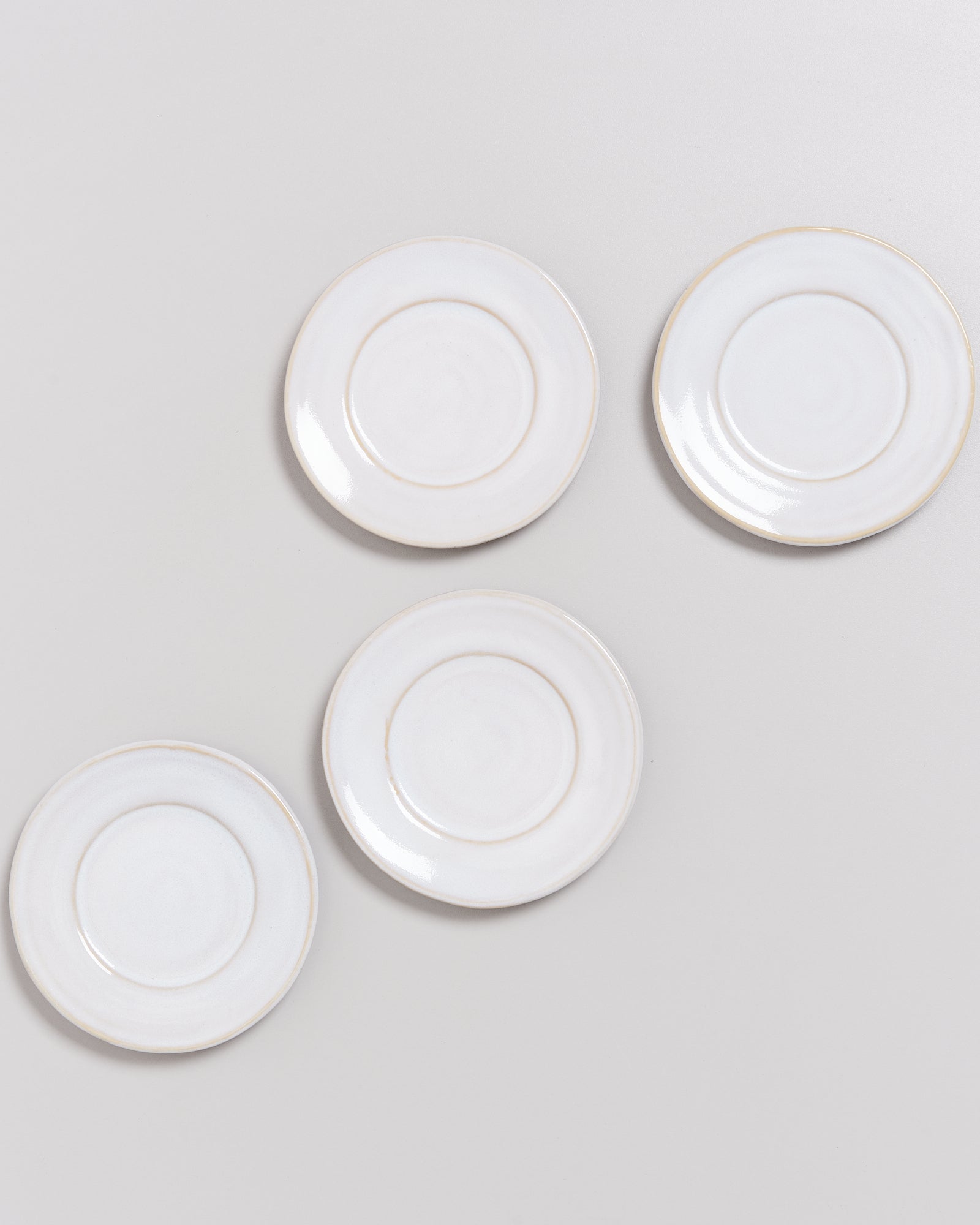 Vier weiße Untertassen auf einem hellgrauen Hintergrund, diagonal angeordnet.