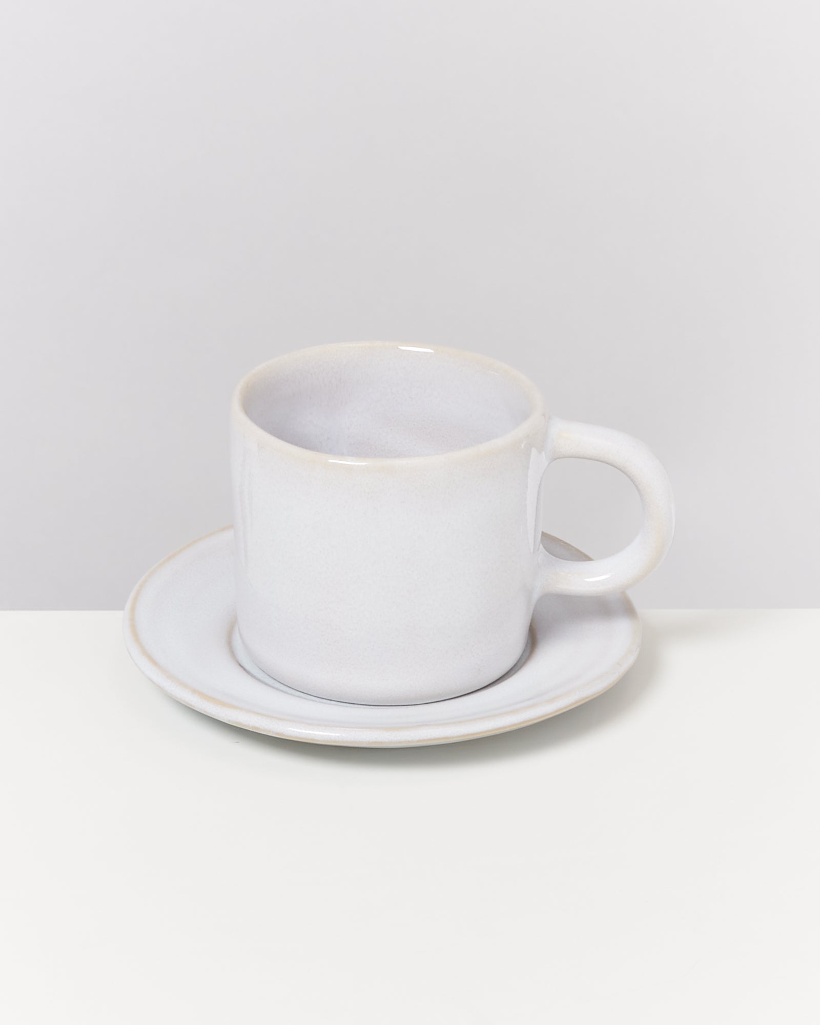 Weiße Tasse mit Unterteller auf einem weißen Hintergrund.