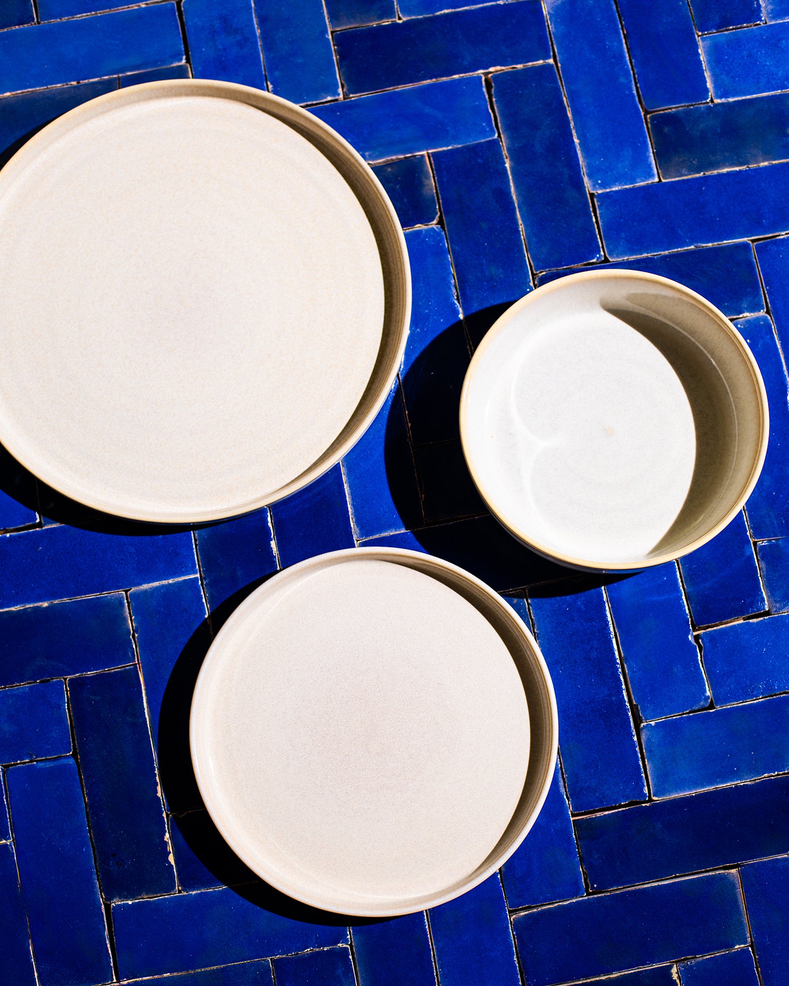 Drei cremefarbene Keramikteller liegen auf blauen, gemusterten Fliesen.