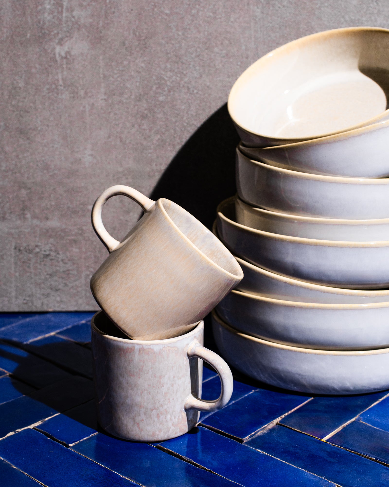 Zwei gestapelte Keramiktassen und ein Stapel Teller auf einem blauen Fliesenuntergrund.