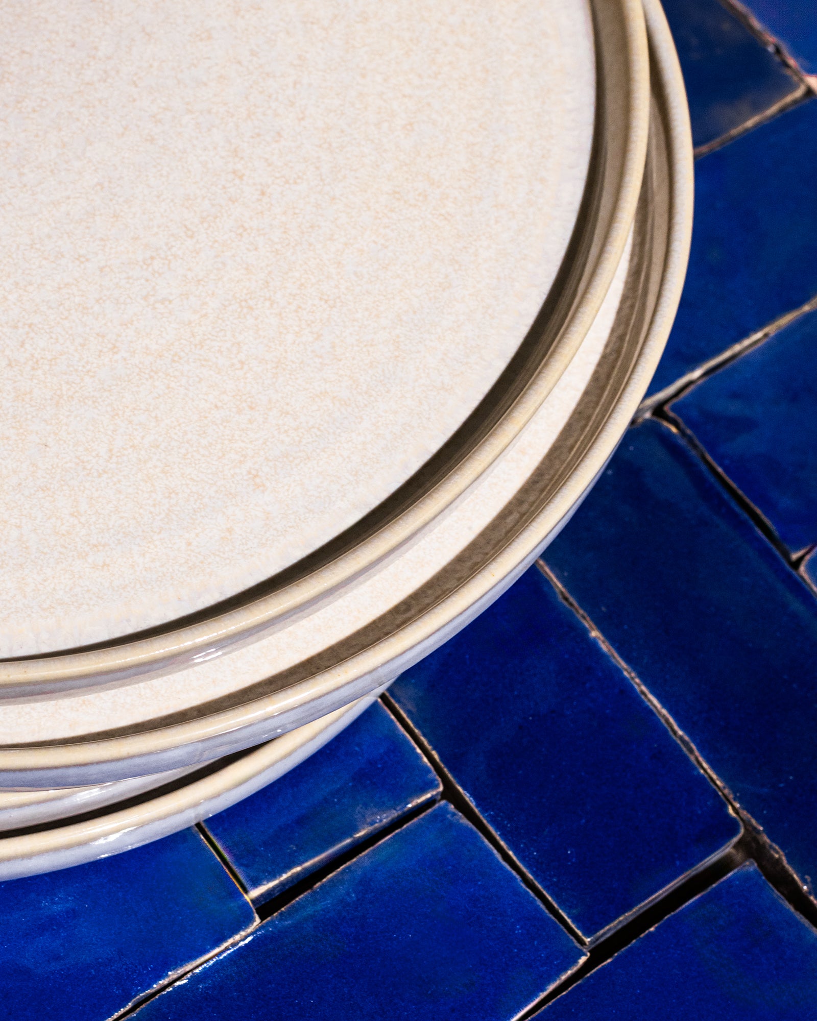 Ein Stapel weißer Teller liegt auf einem tiefblau gefliesten Untergrund.