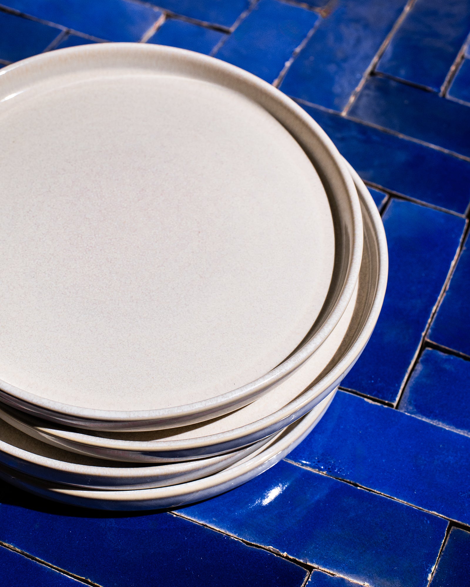 Ein Stapel cremefarbener Teller liegt auf einem blauen Fliesenboden.