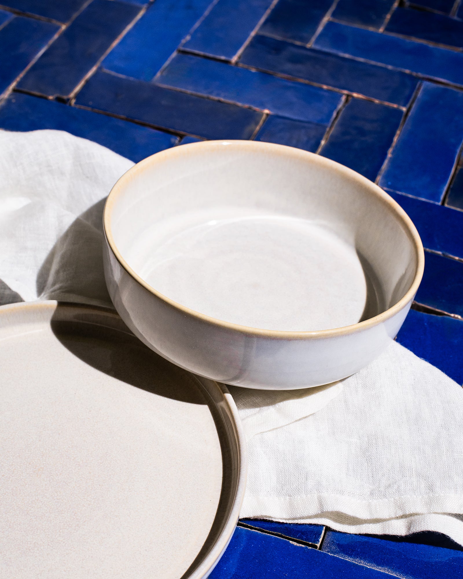 Zwei weiße Keramikschüsseln auf blauen Fliesen mit einem weißen Tuch darunter platziert.