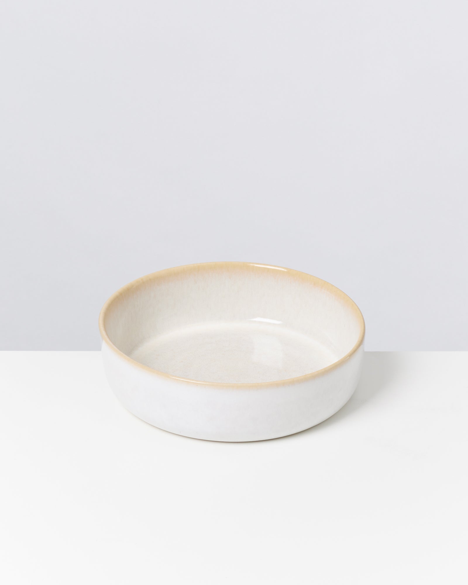 Eine flache, runde, cremefarbene Schale mit beigem Rand auf weißem Hintergrund.