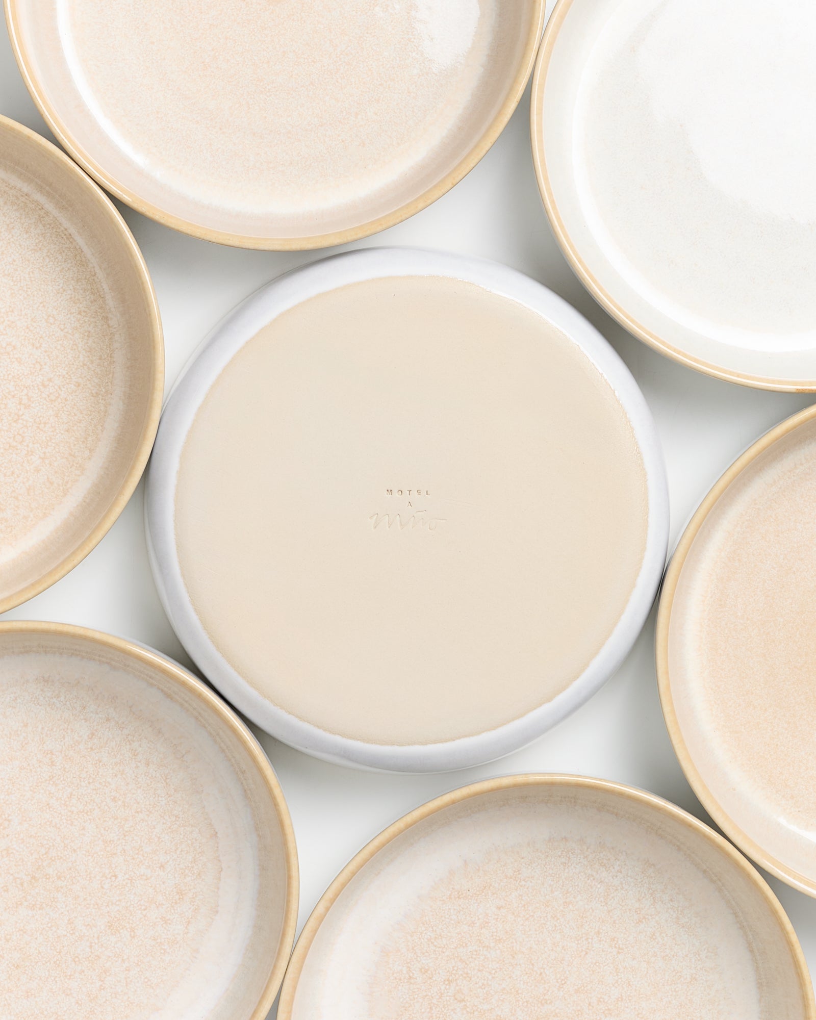 Sieben beigefarbene Keramikteller liegen auf einer weißen Oberfläche, einer mit der Unterseite nach oben.