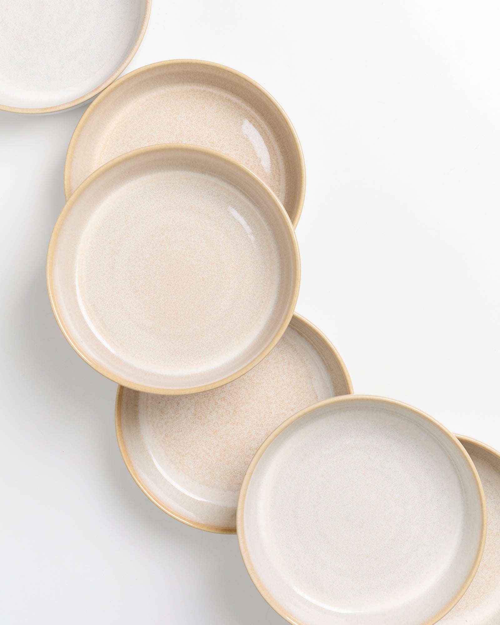 Fünf cremefarbene Keramikteller überlappen sich in einer diagonalen Linie auf weißem Hintergrund.