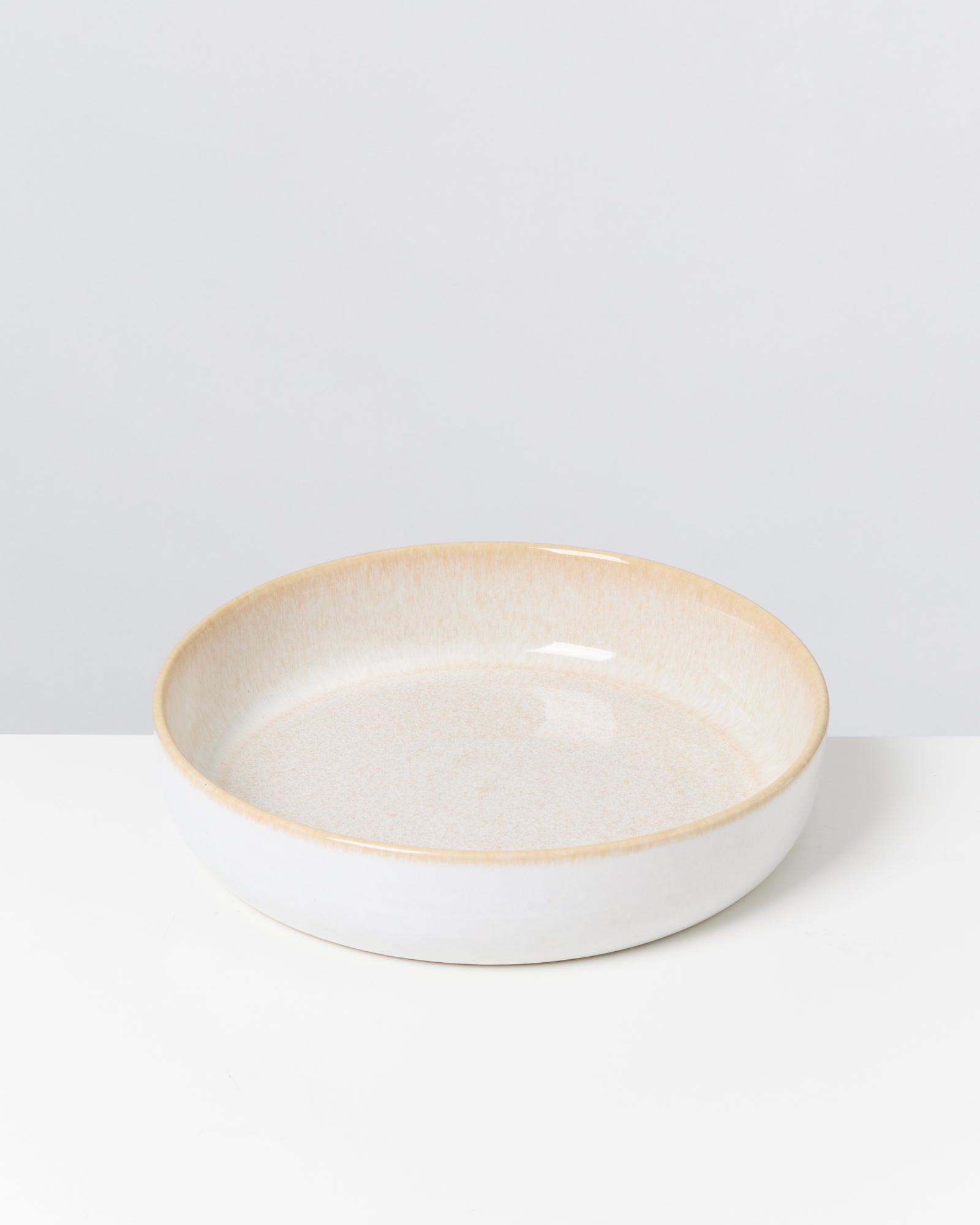 Flacher Keramikteller mit beiger Innenseite auf weißem Hintergrund.