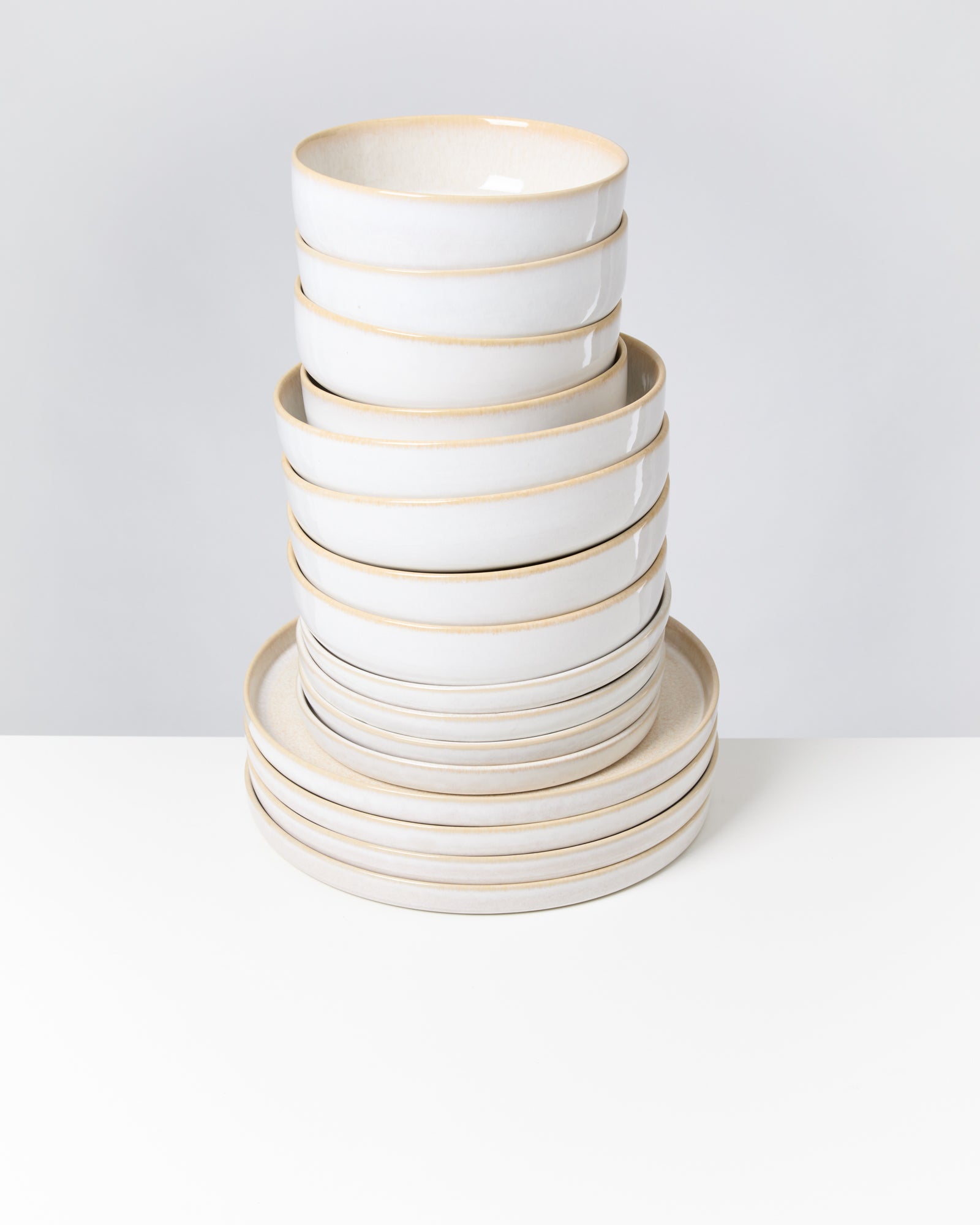 Ein Stapel aus weißen Schalen und Tellern auf einem weißen Tisch vor einem grauen Hintergrund.