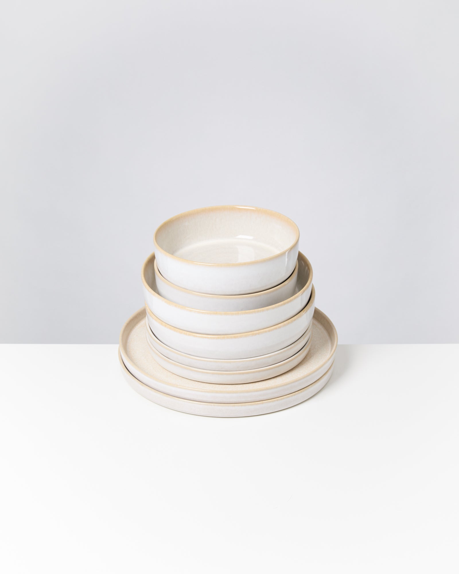 Ein Stapel von vier weißen, runden Schalen und Tellern auf einem weißen Tisch vor einem grauen Hintergrund.