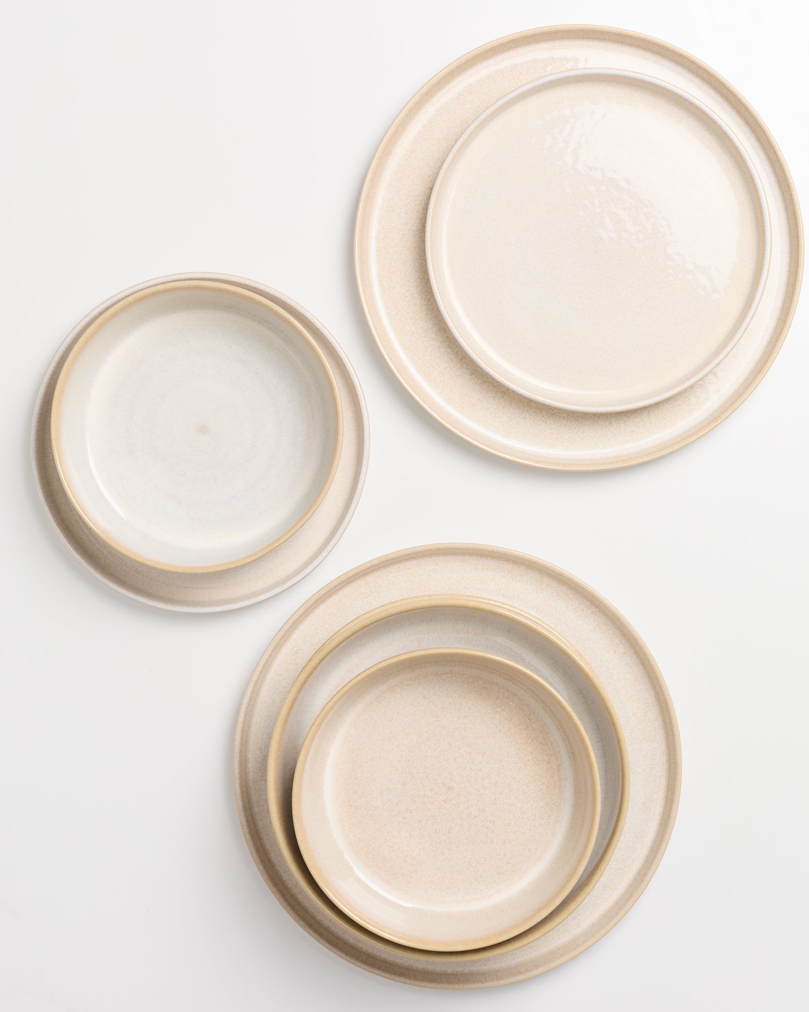 Beiges Keramikgeschirr auf weißem Hintergrund, bestehend aus drei übereinander liegenden Tellern und einer kleinen Schale.