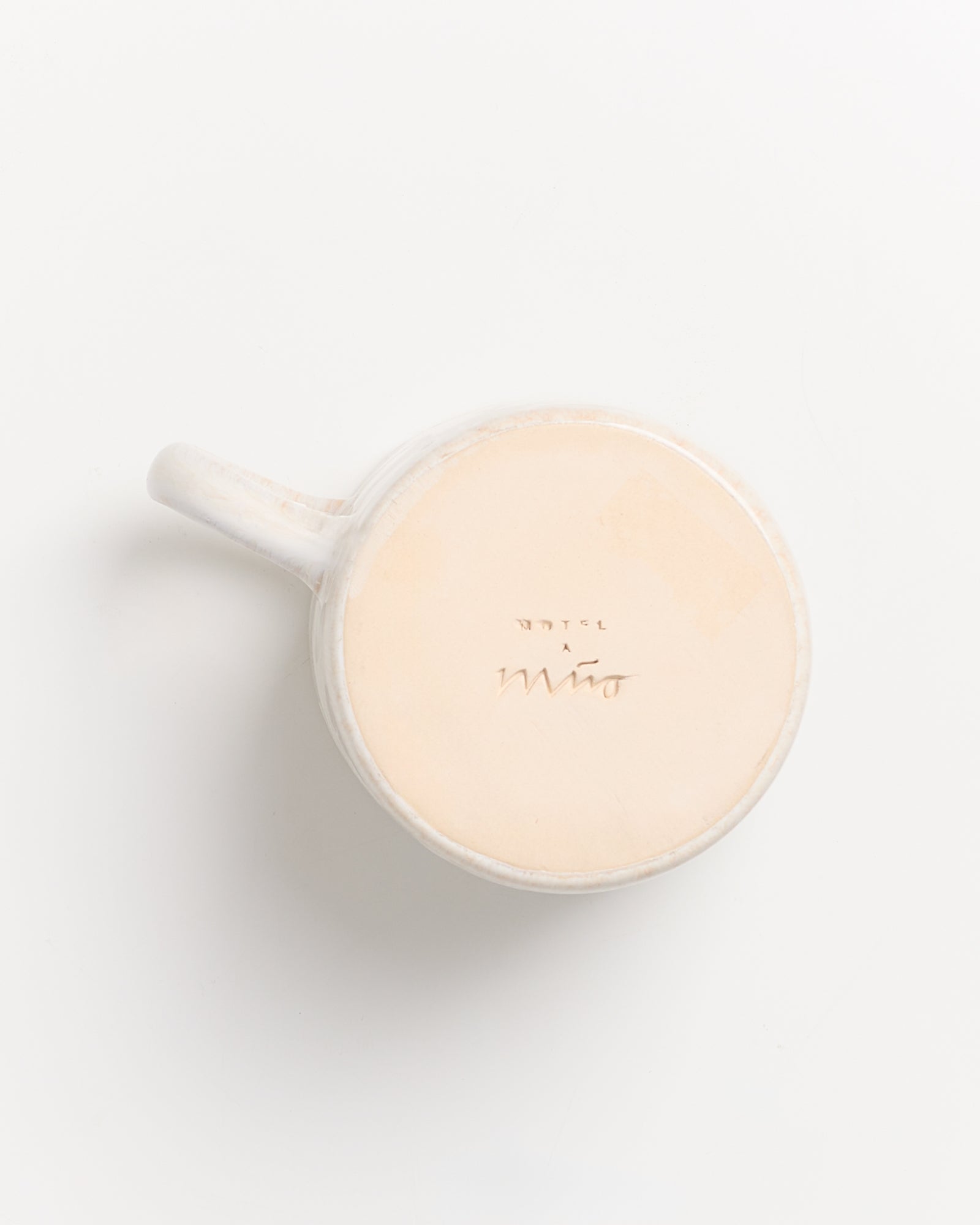 Weiße Tasse aus Keramik, von unten fotografiert, mit eingeprägter Schrift auf dem Boden.
