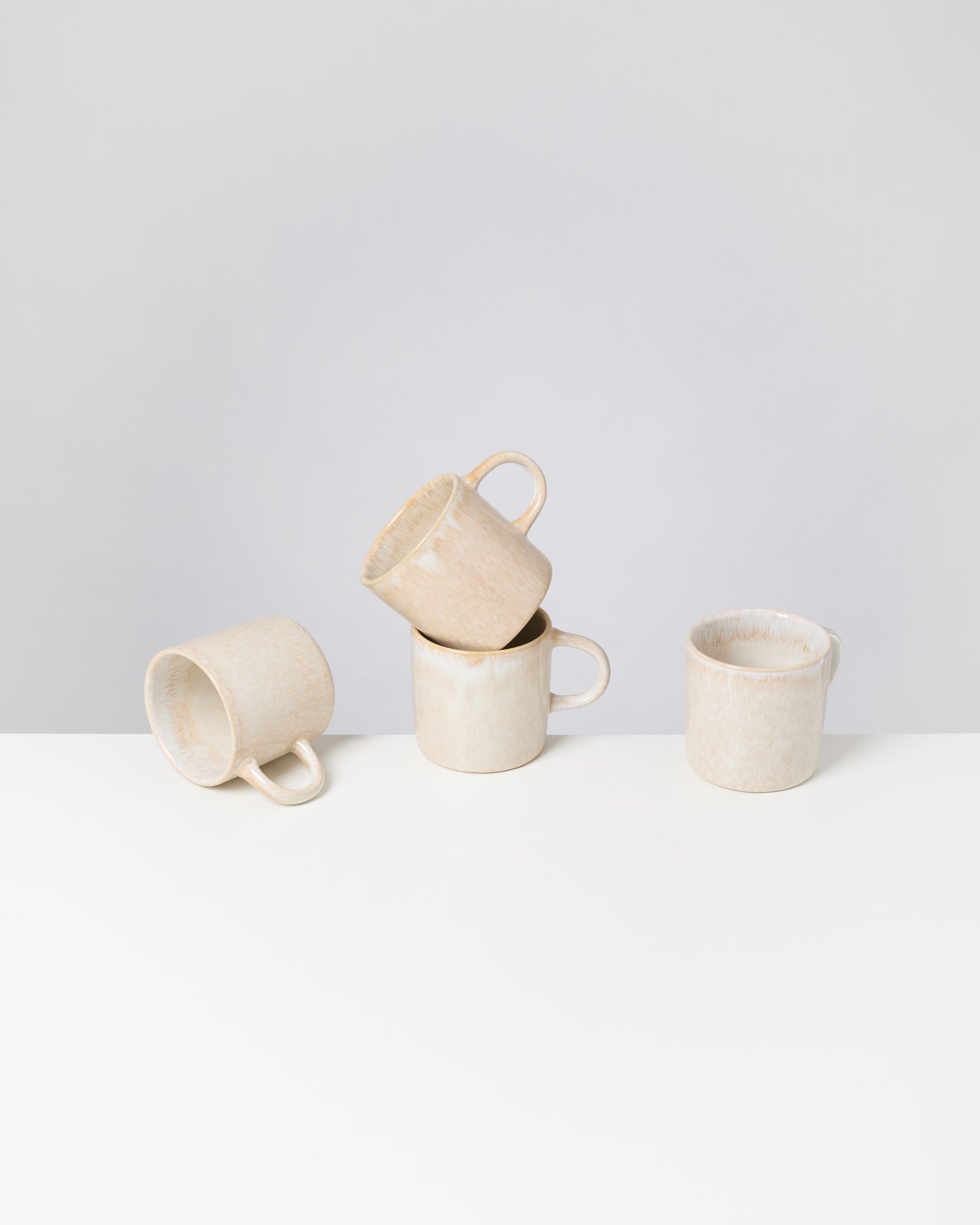Vier beige Tassen aus Keramik stehen auf einem weißen Tisch, drei davon sind gestapelt.