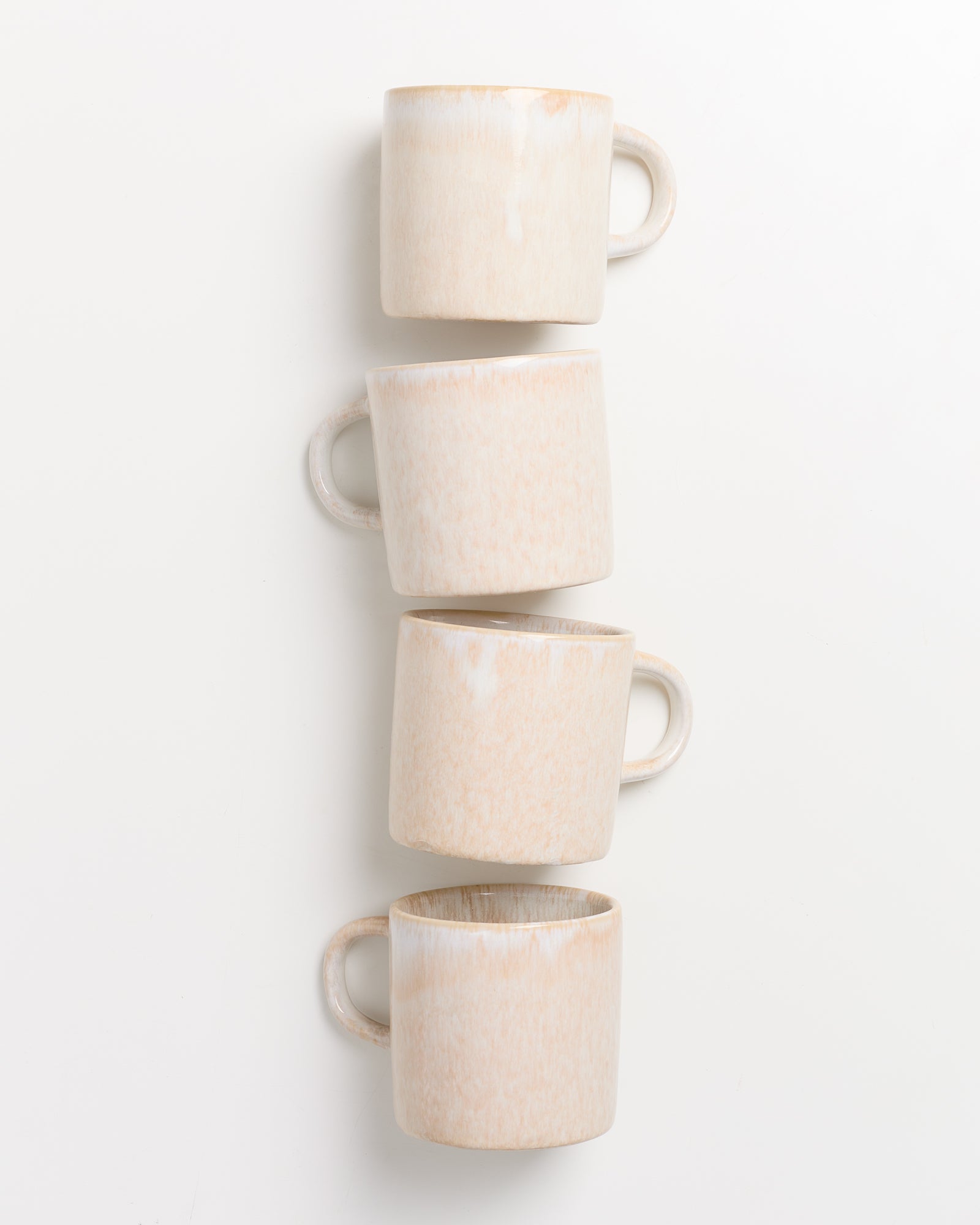 Vier sandfarbene Tassen mit Henkeln sind vertikal übereinander gestapelt auf weißem Hintergrund.